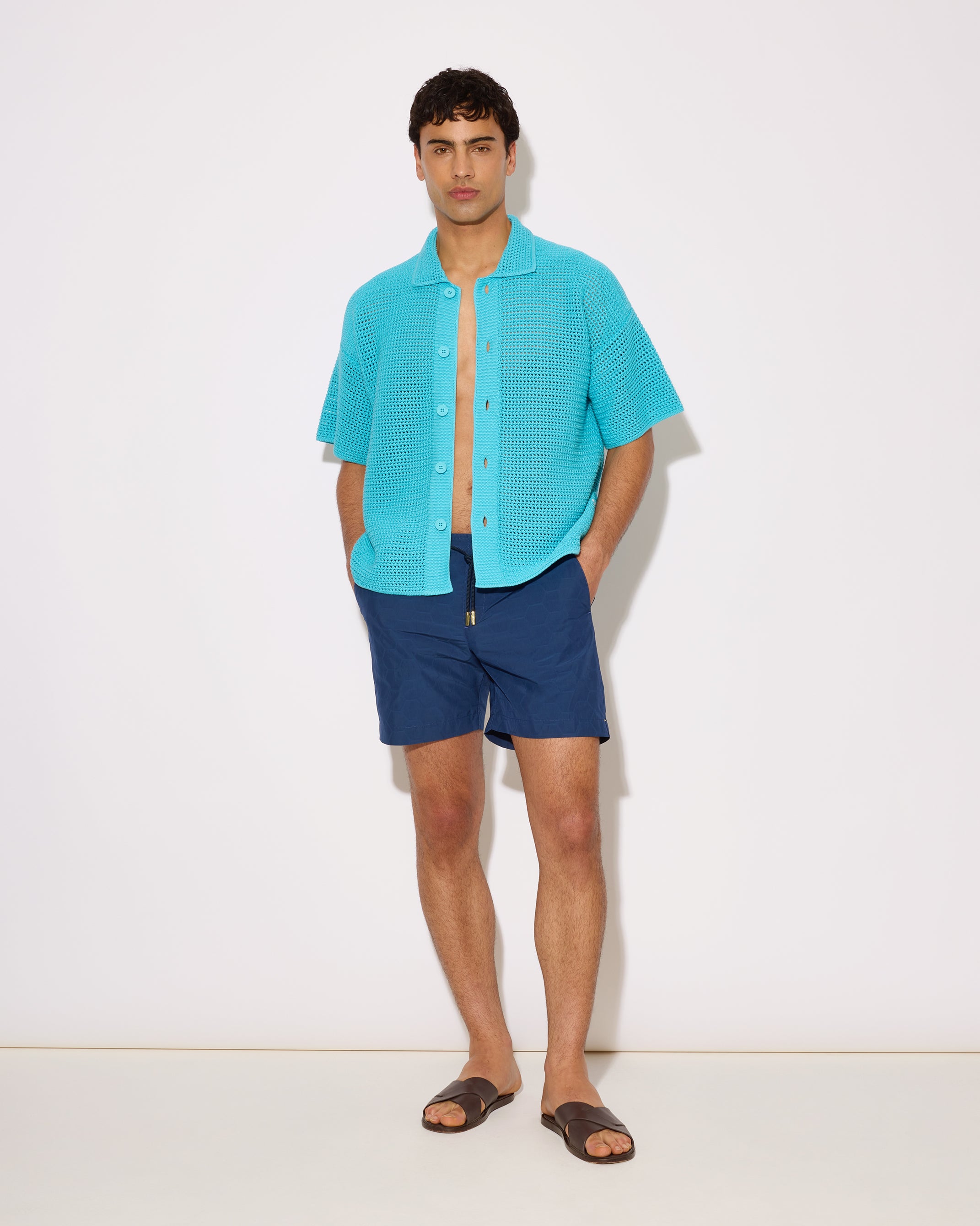 Man wearing a turquoise shirt and blue shorts on a white background
