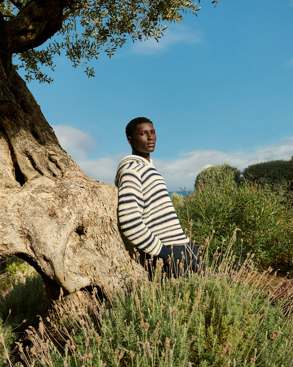 Man wearing black and white stripe knitted hoodie leaning against a tree trunk
