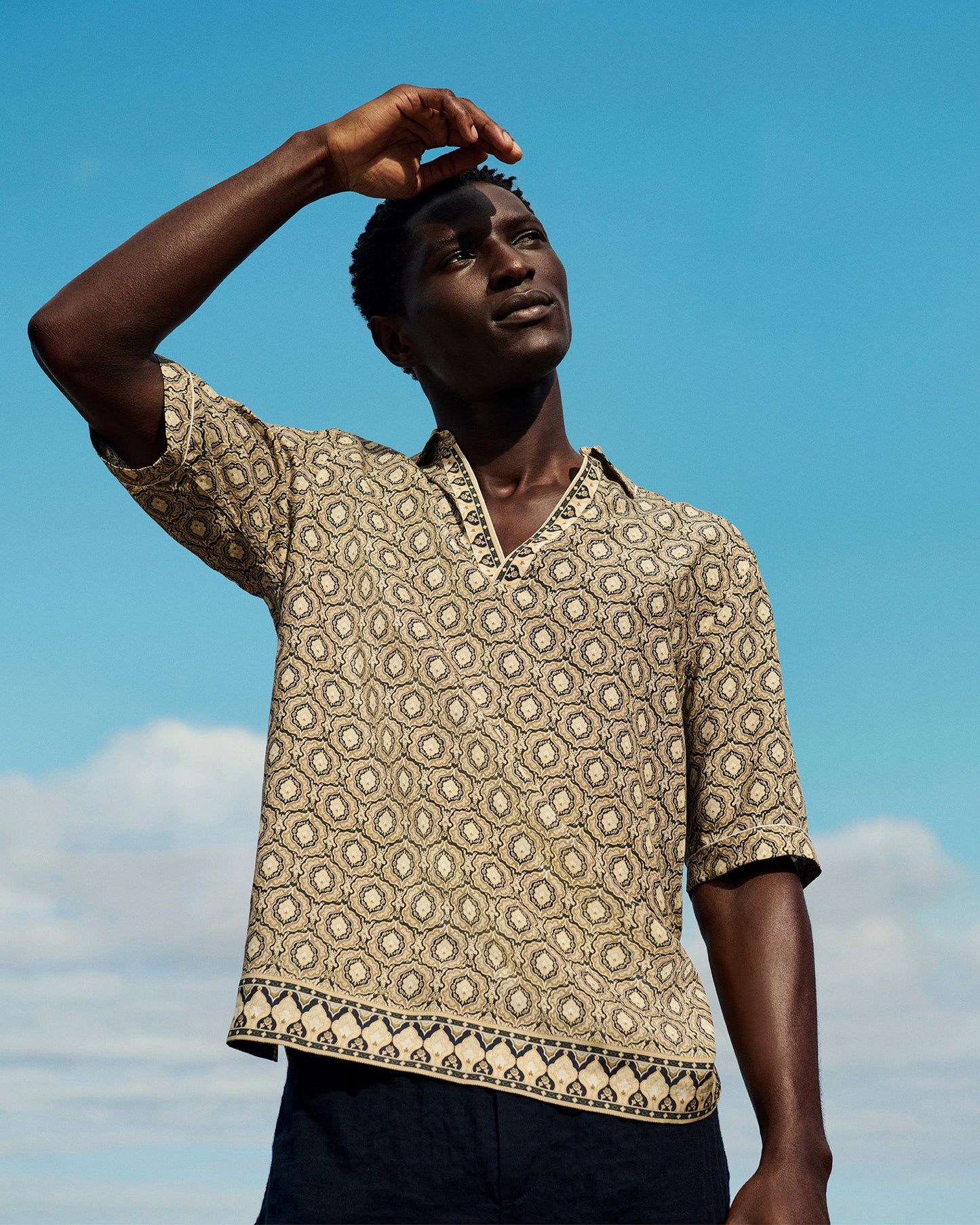 Man wearing a patterned shirt against a blue sky