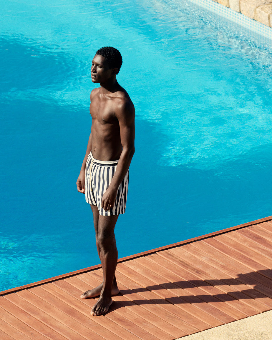 Man standing by a pool wearing striped swim shorts