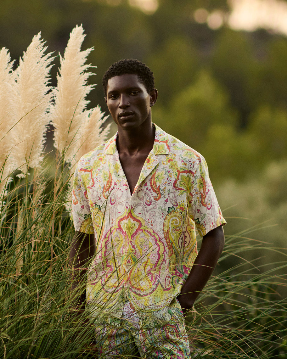 Man wearing a colorful patterned shirt and pants standing in tall grass.