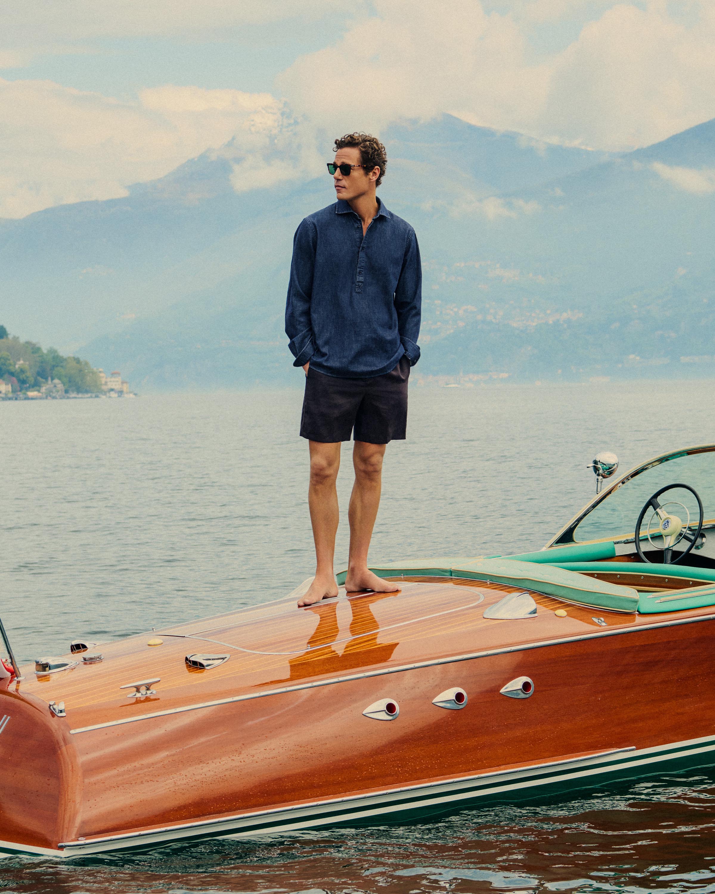 Man standing on a wooden boat with mountains in the background