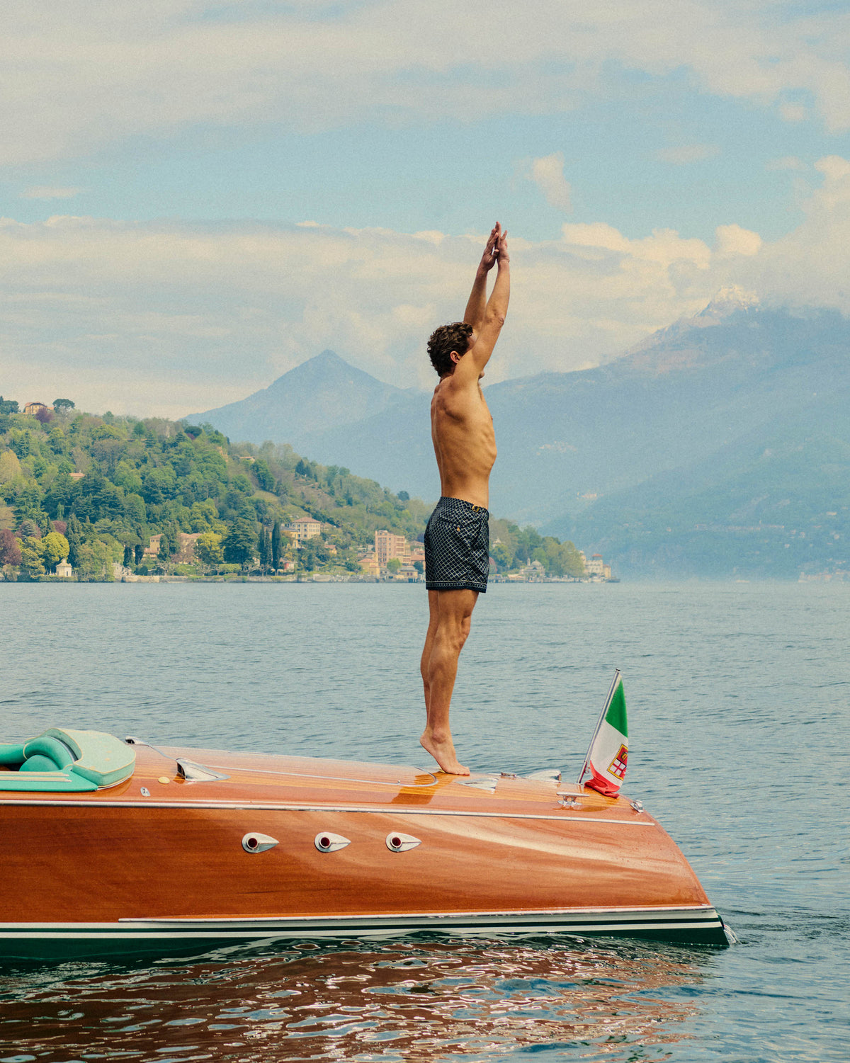 Man standing on a boat with arms raised over a lake with mountains in the background