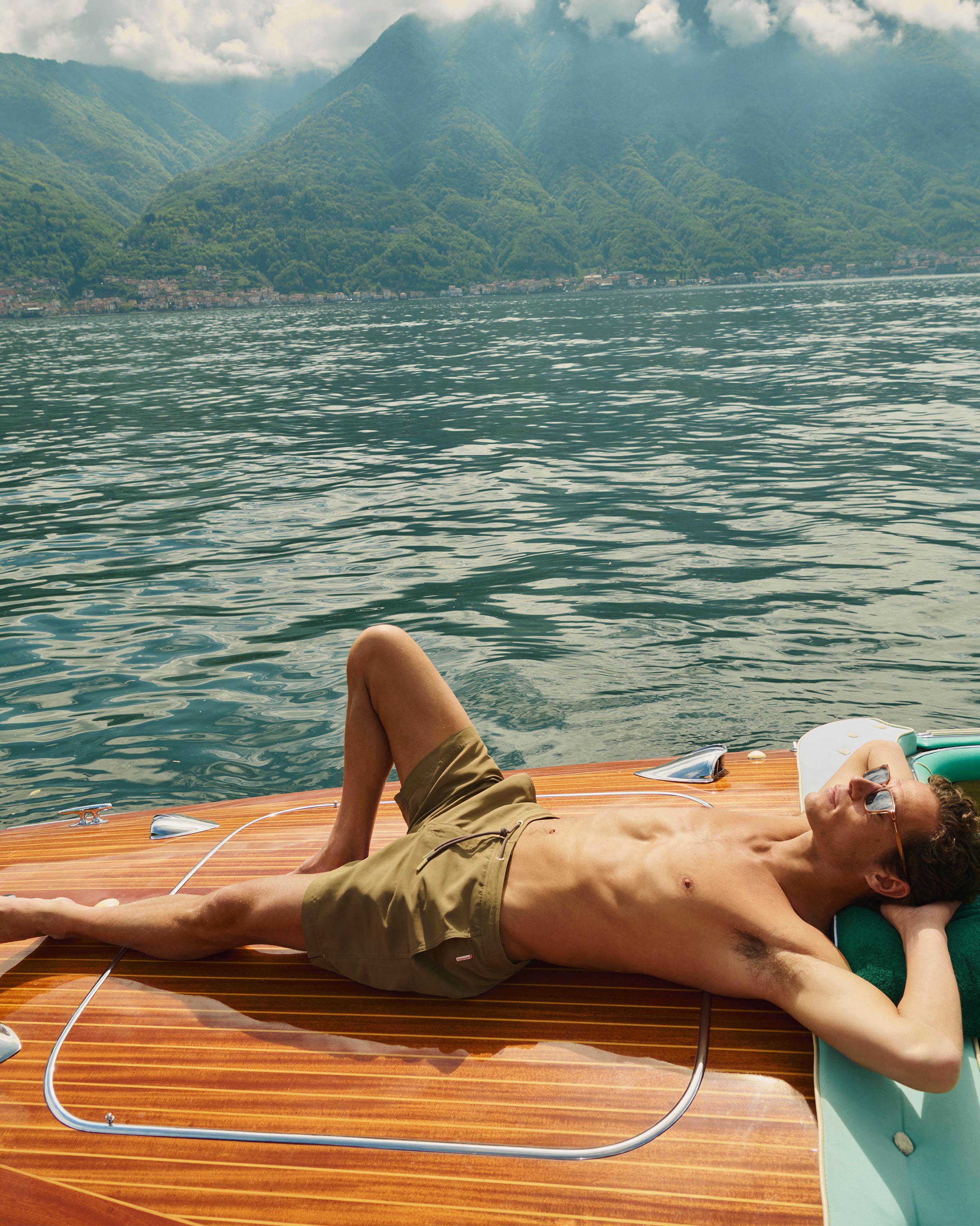 Man lying on a wooden boat on a lake with mountains in the background