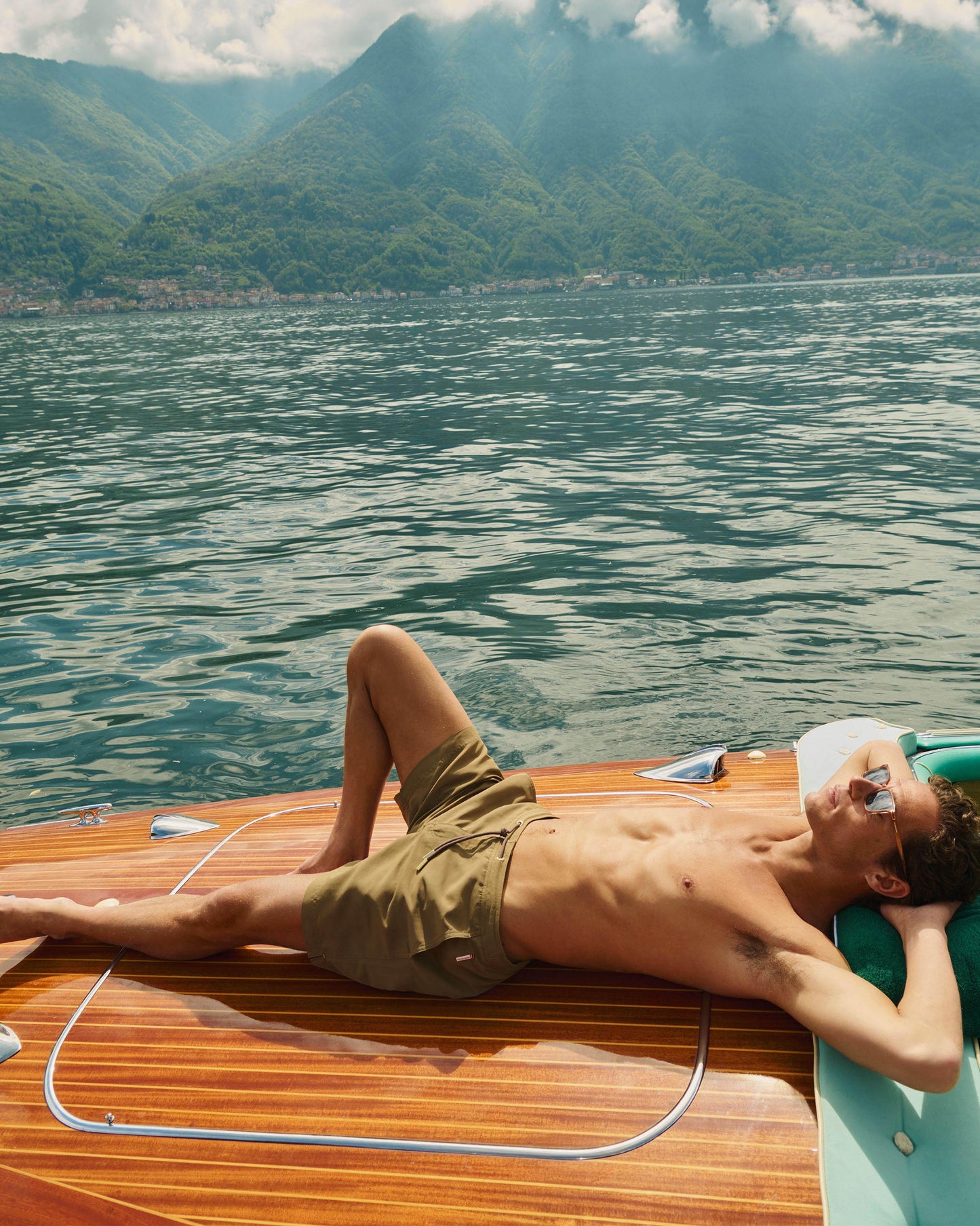 Man lying on a wooden boat on a lake with mountains in the background