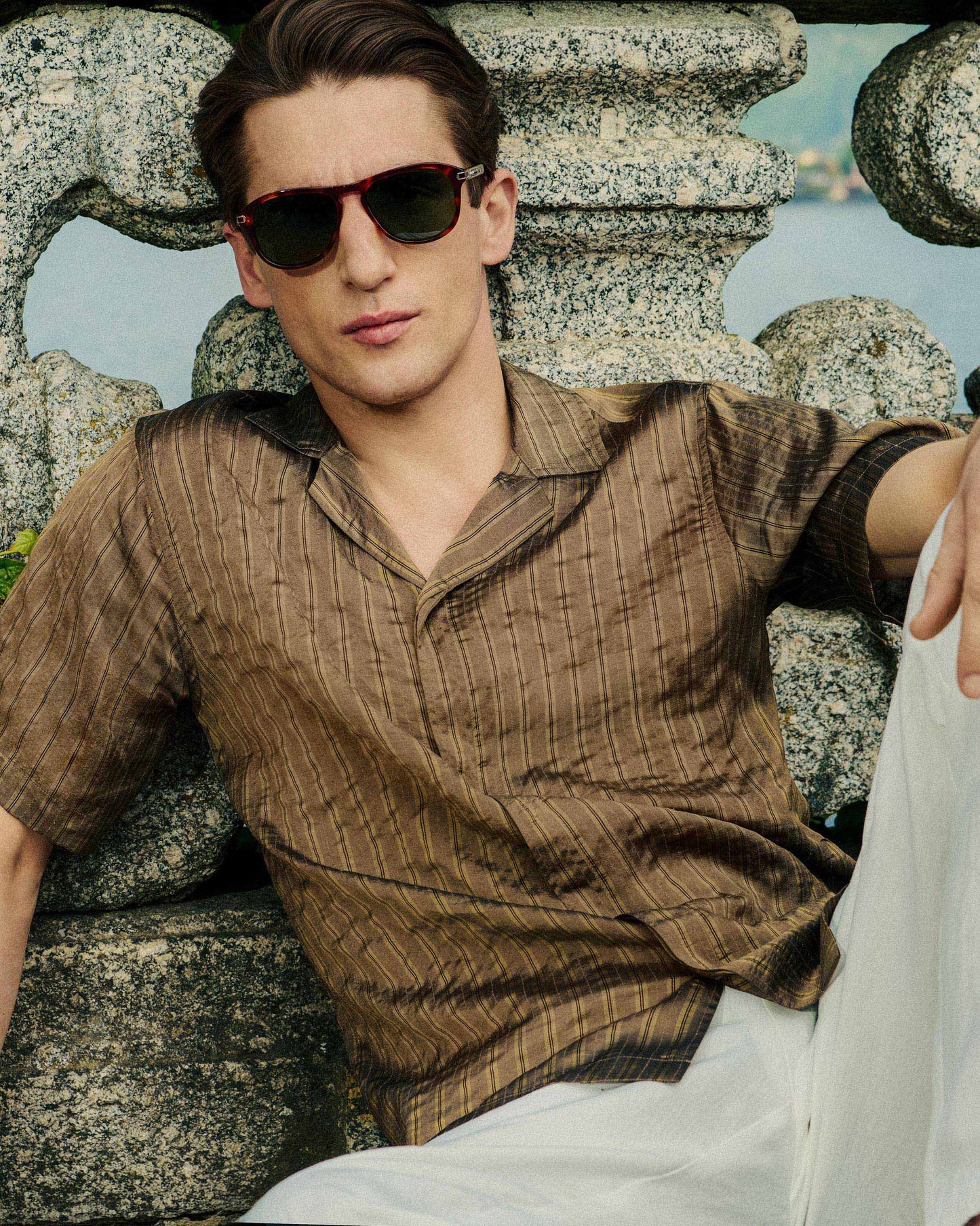 Man wearing sunglasses and a brown shirt sitting on stone steps.
