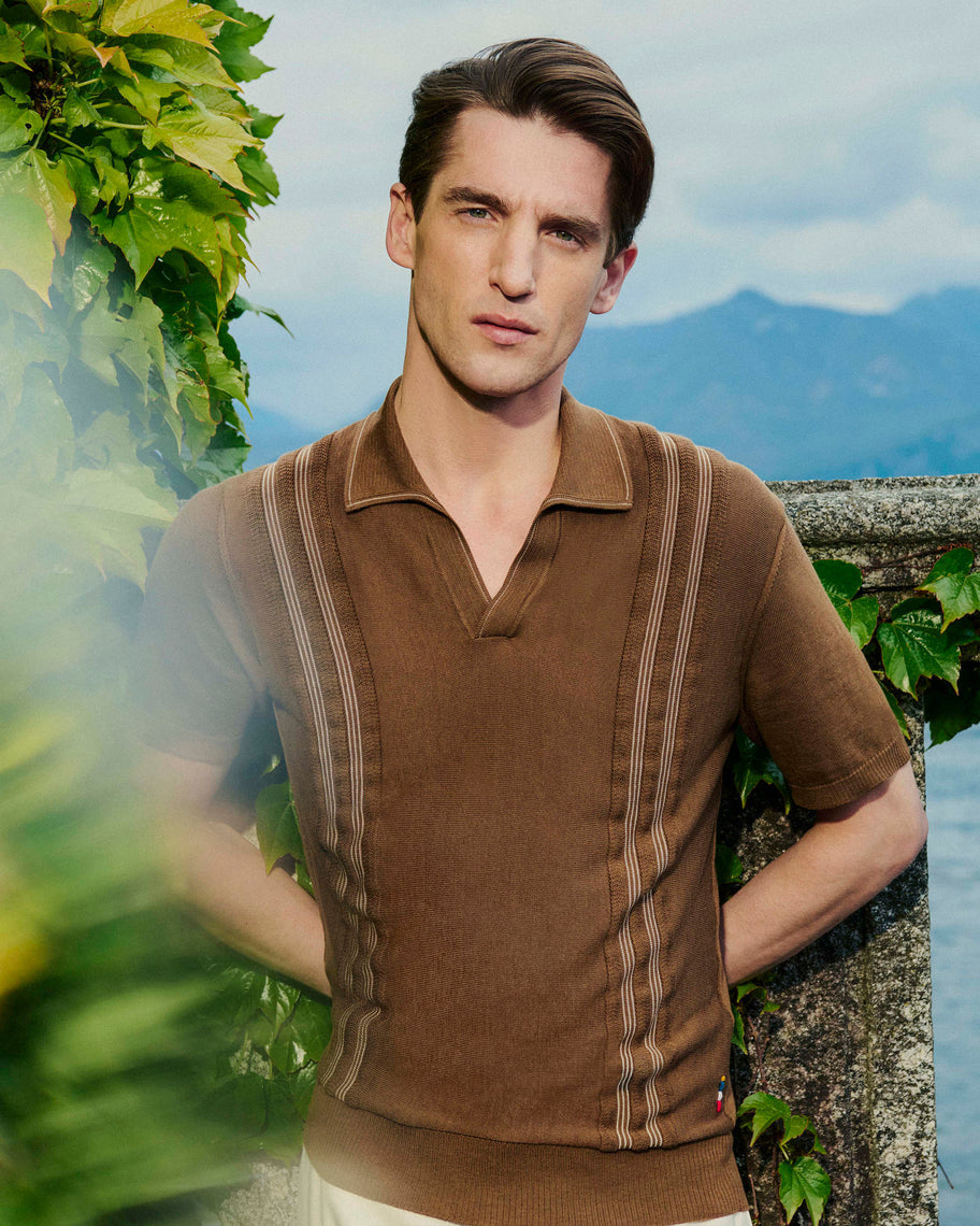 Man wearing a brown polo shirt with a scenic background
