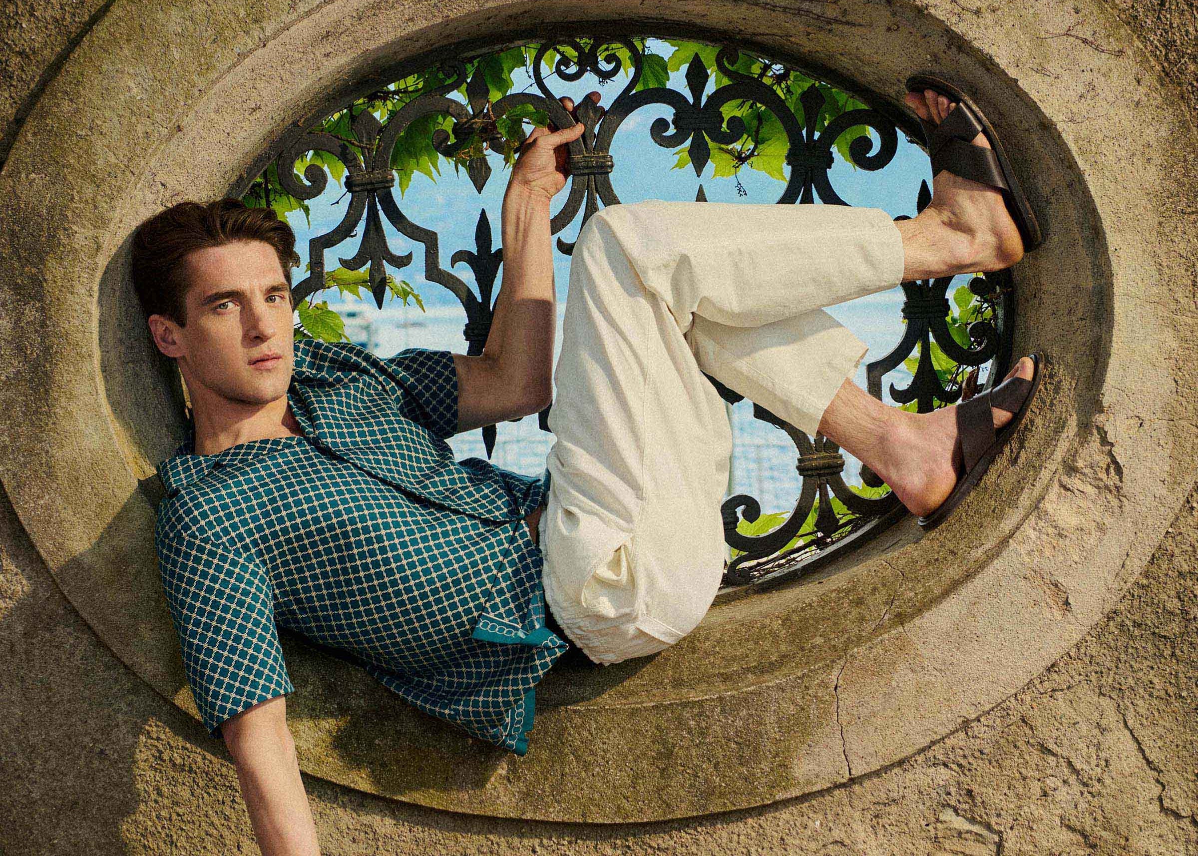 Person lying inside a circular stone window with a decorative iron grille.