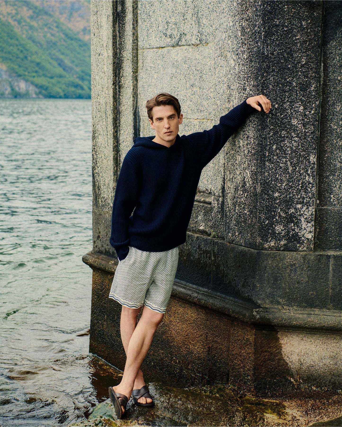 Man leaning against a stone wall by a body of water