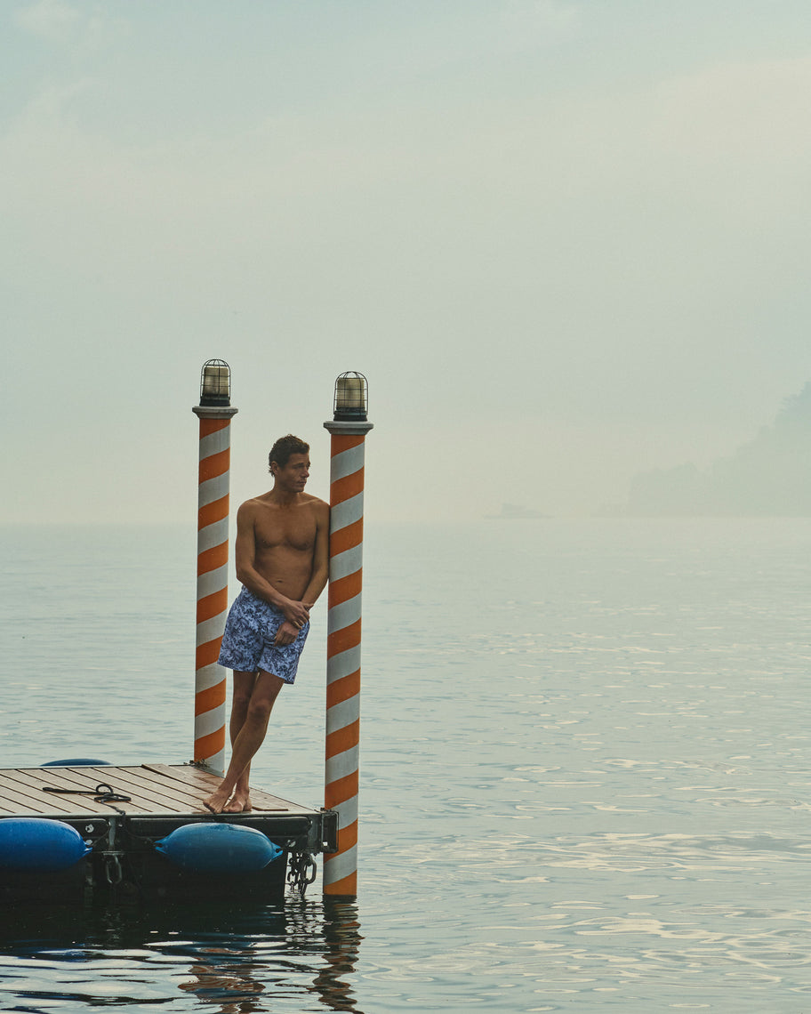 Man standing on a dock with striped posts, surrounded by water and sky.