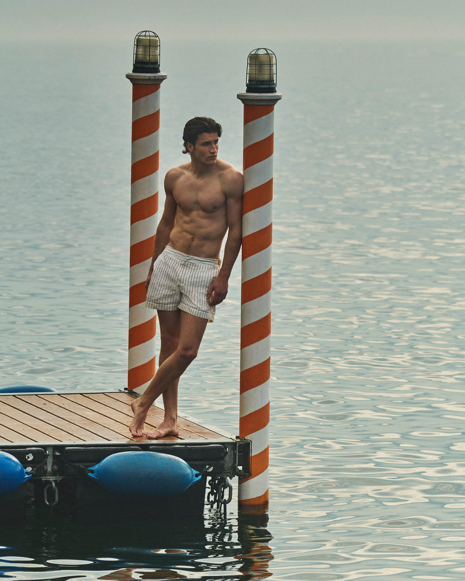 Man standing on a dock with striped posts and blue buoys, water background