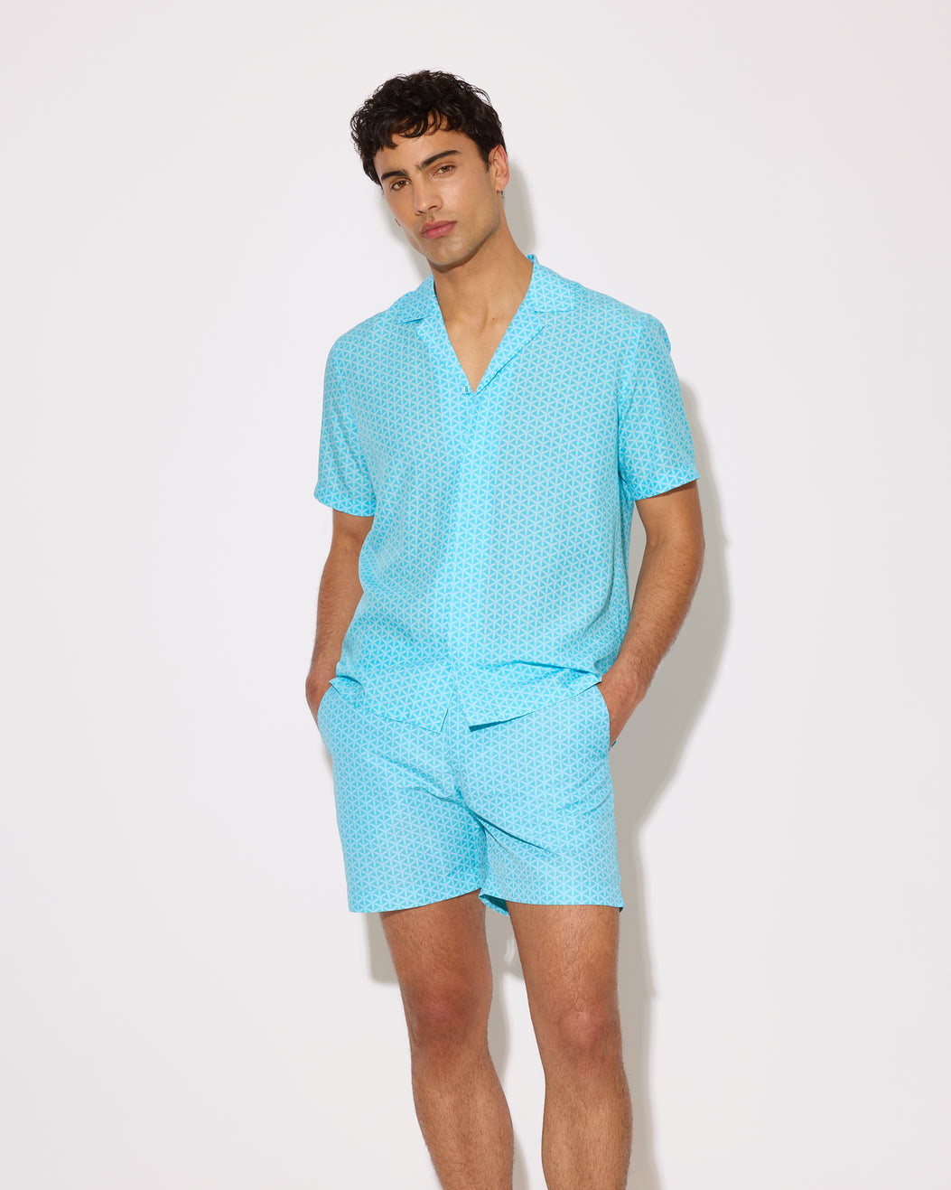 Man wearing a light blue patterned shirt and shorts set on a white background
