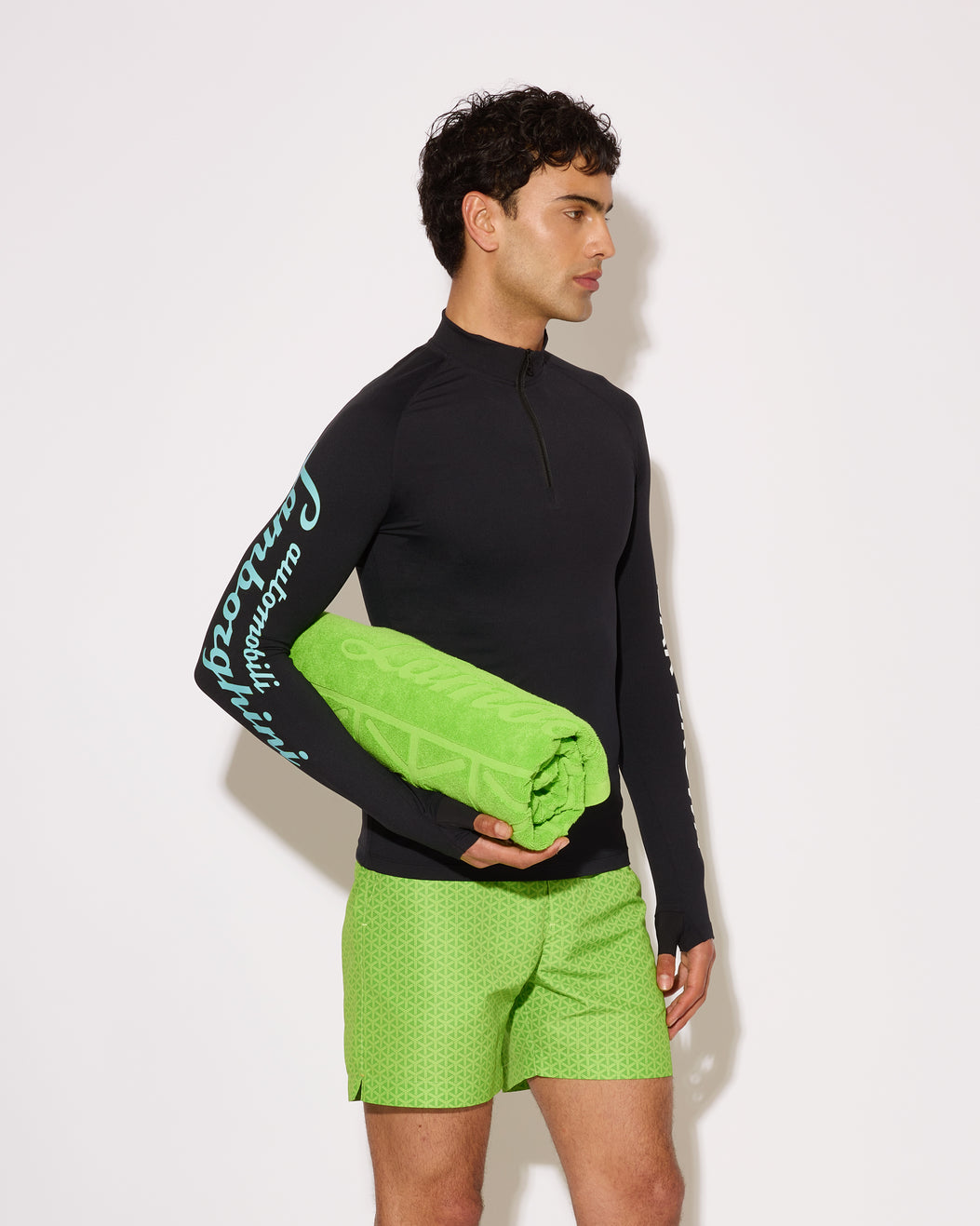 Person wearing a black long-sleeve shirt and green shorts holding a green towel against a white background