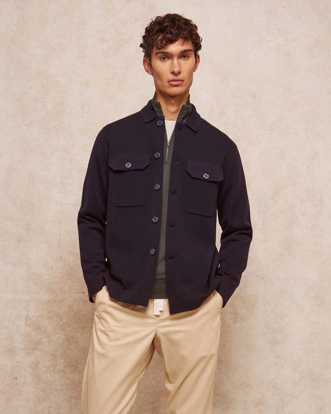 Man wearing a dark jacket and beige pants against a neutral background