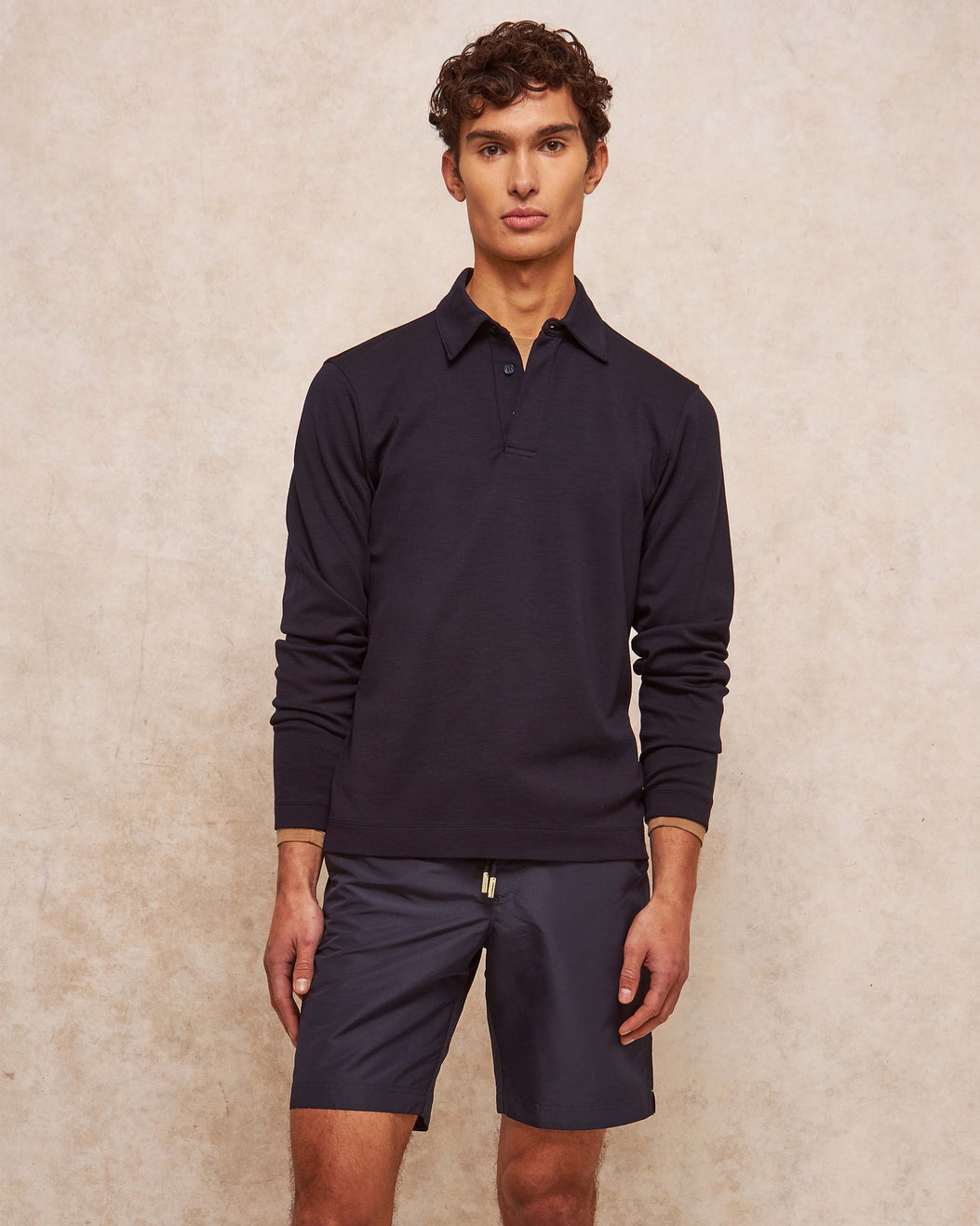Man wearing a dark long-sleeve shirt and shorts against a beige background