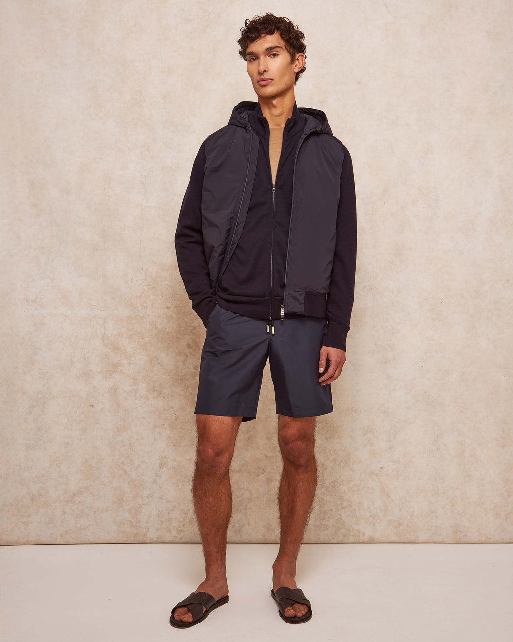 Man wearing a navy jacket and shorts against a beige wall