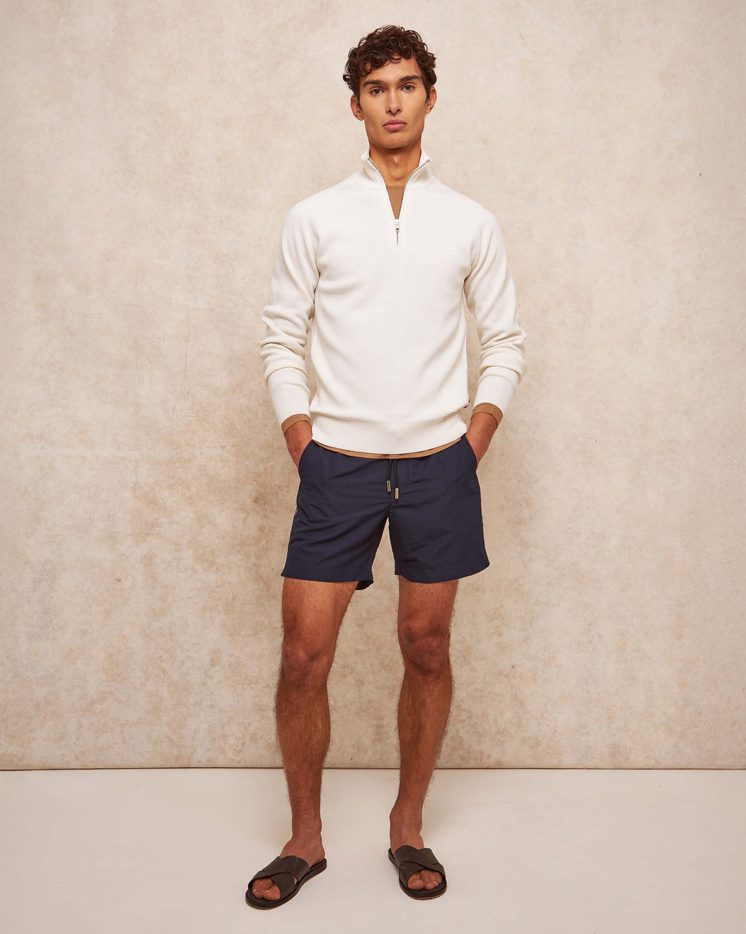 Man wearing a white sweater and navy shorts against a beige background