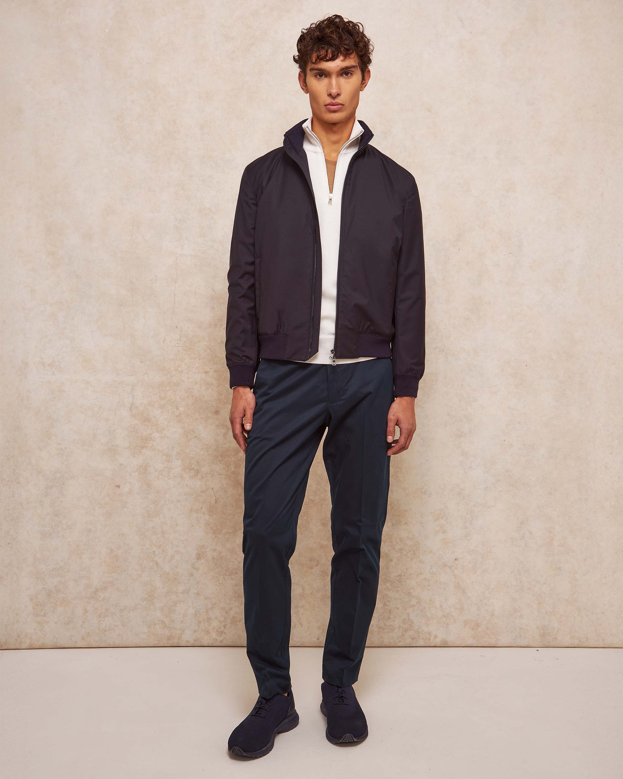 Man wearing a navy jacket and pants against a beige background