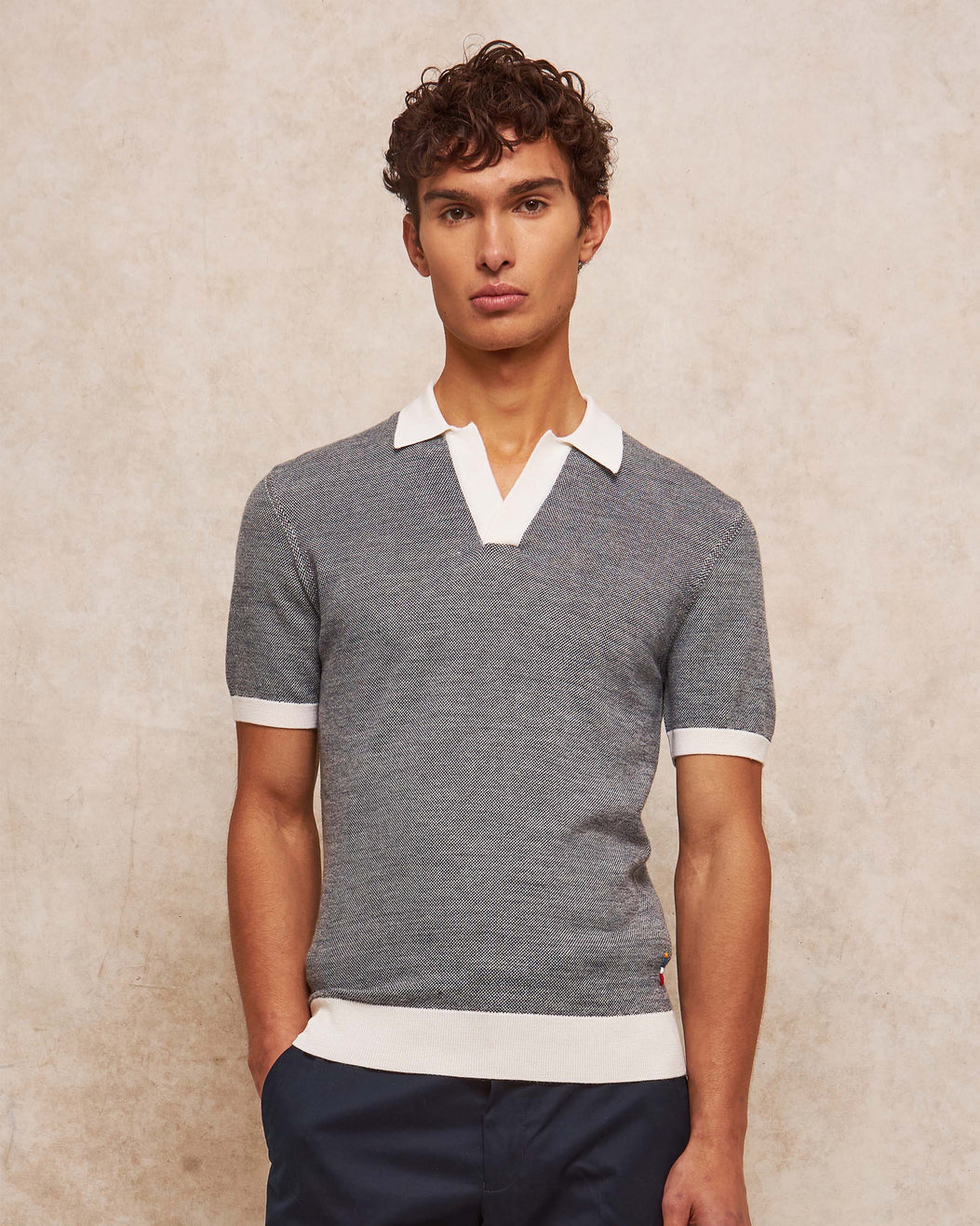 Man wearing a gray short-sleeve sweater with white trim against a beige background