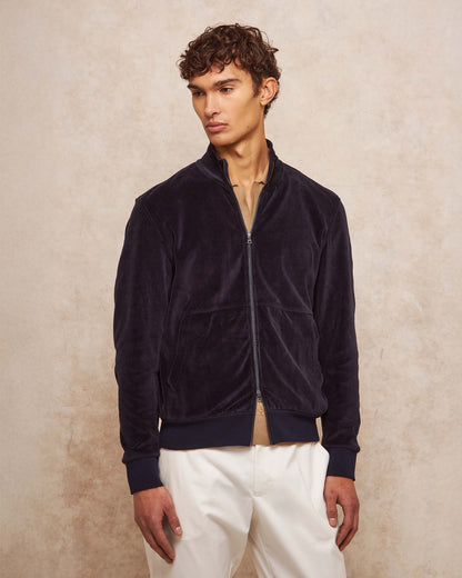 Man wearing a navy blue jacket and white pants against a beige background