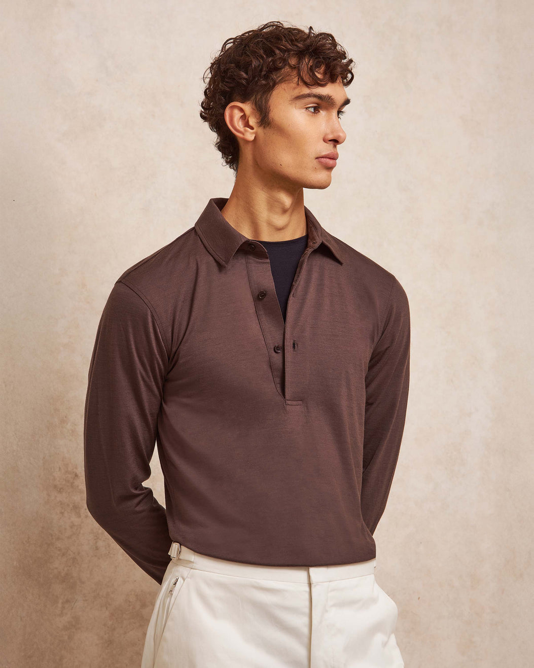 Man wearing a brown long-sleeve polo shirt against a beige background