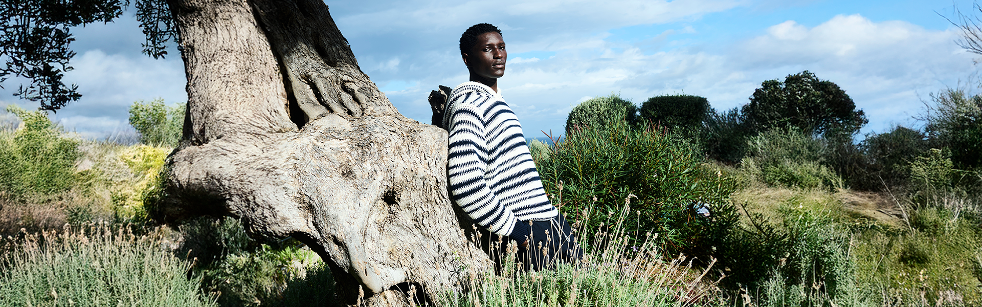 Man leaning against a tree wearing a navy and white striped knitted hoodie