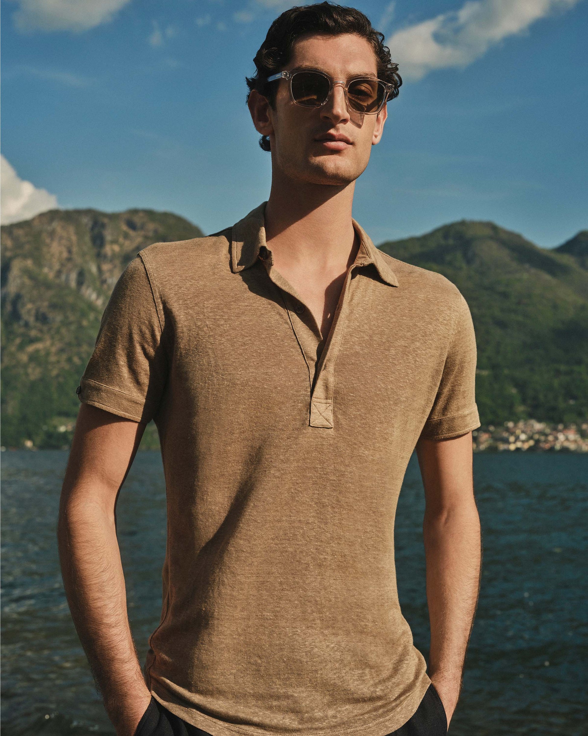 Man wearing a brown polo shirt by a lake with mountains in the background