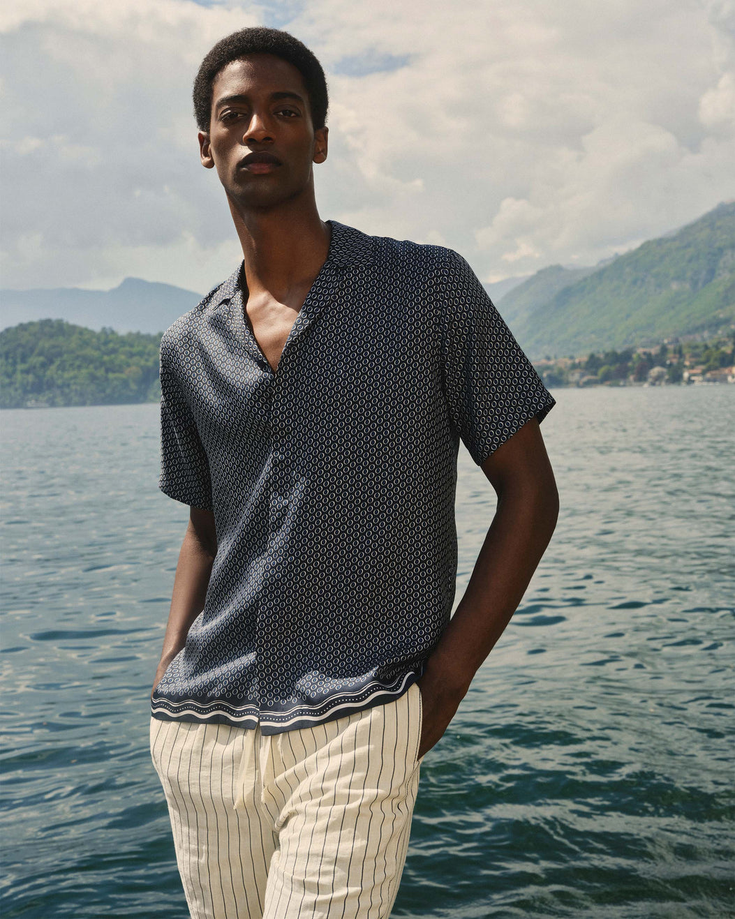 Man standing by a lake with mountains in the background