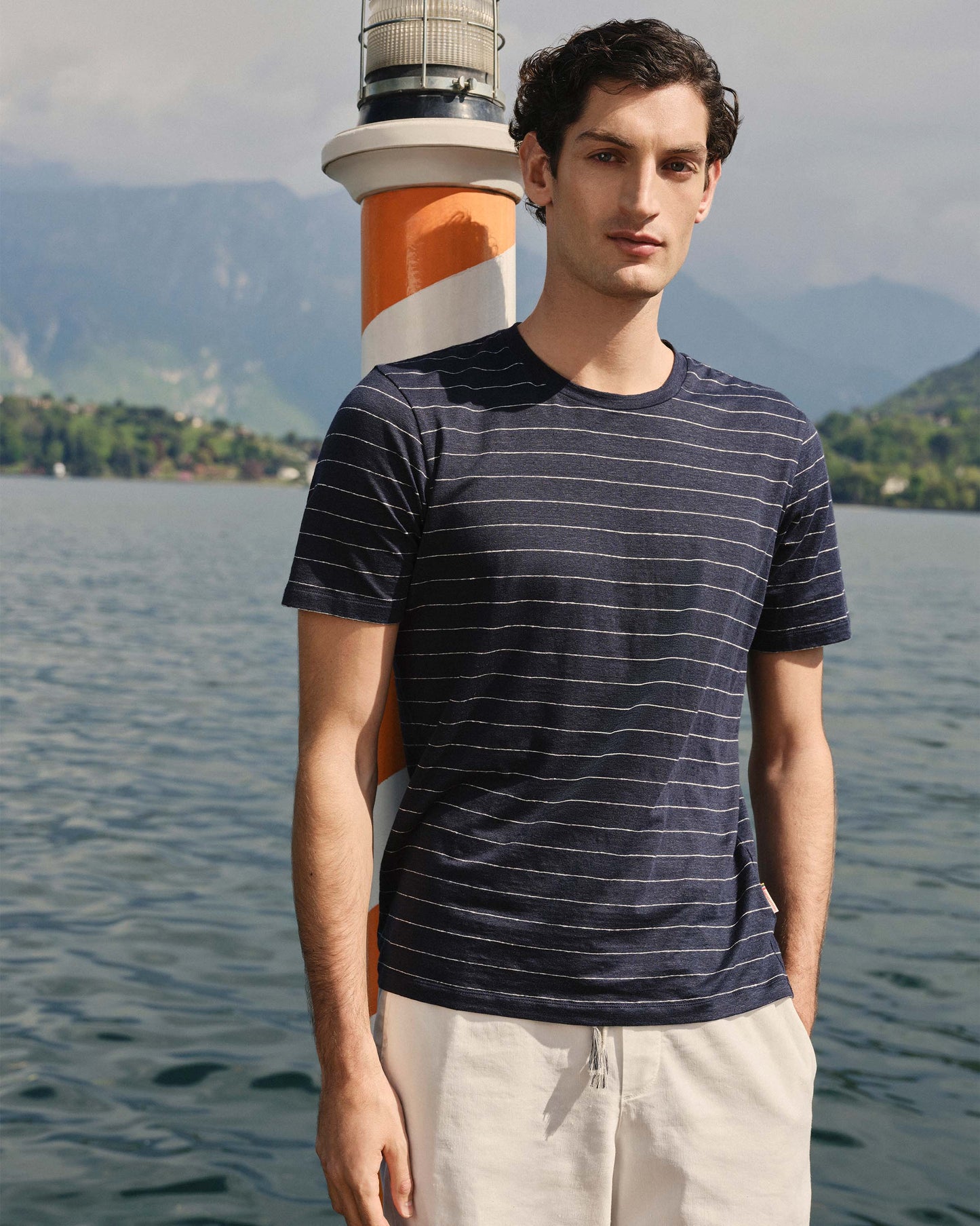 Man wearing a striped shirt with a lighthouse in the background by a lake