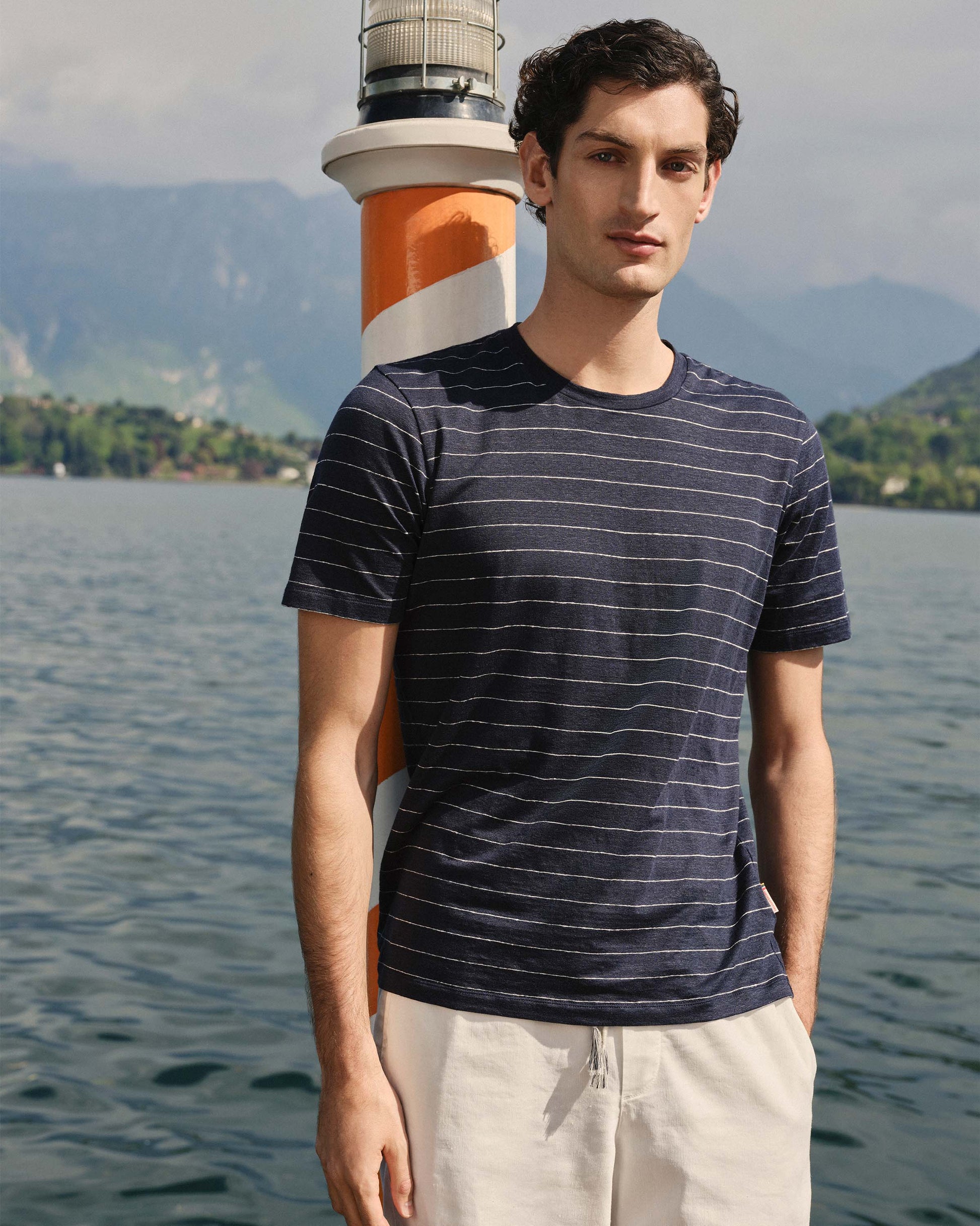Man wearing a striped shirt with a lighthouse in the background by a lake