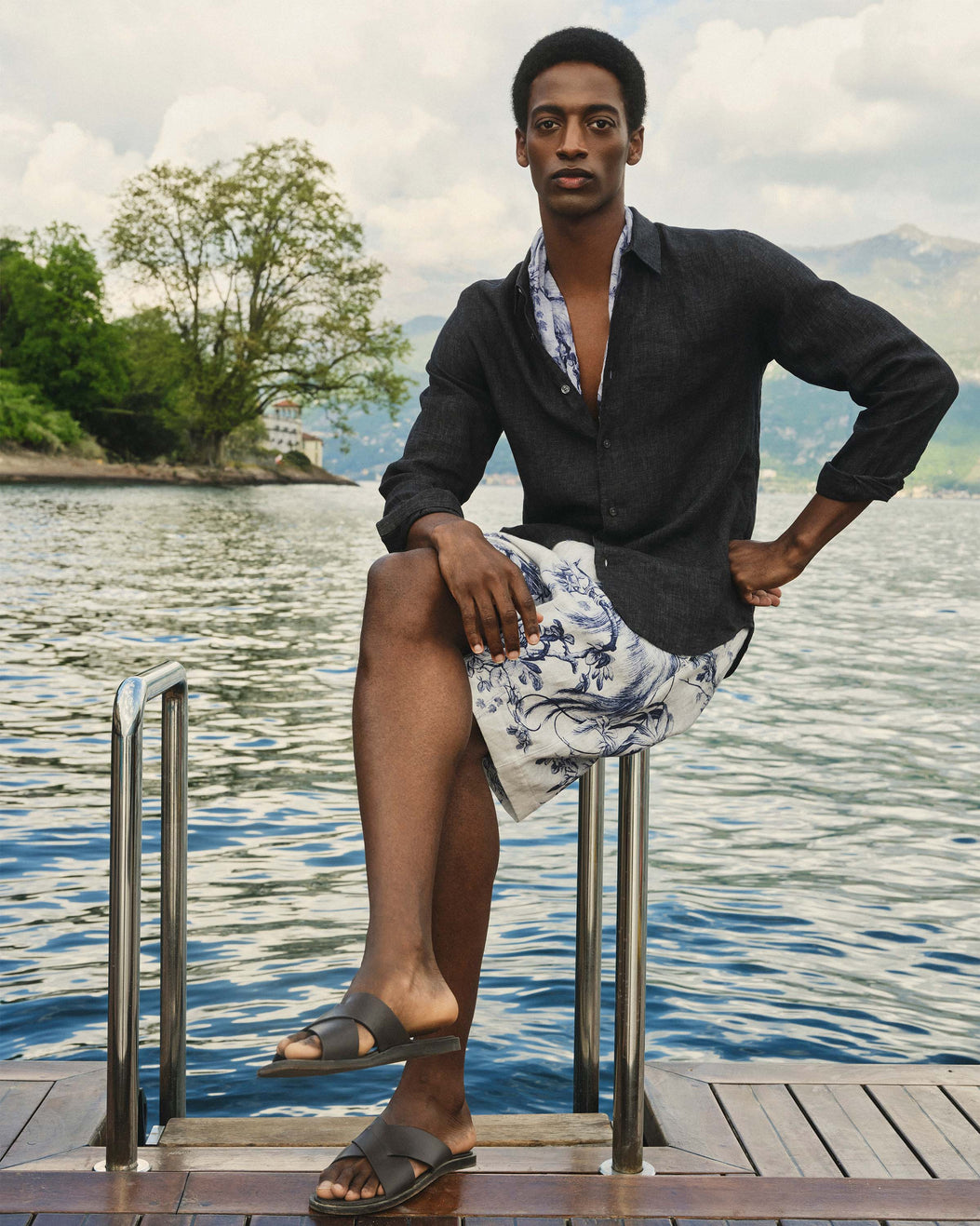 Man sitting on a dock by a lake with mountains in the background