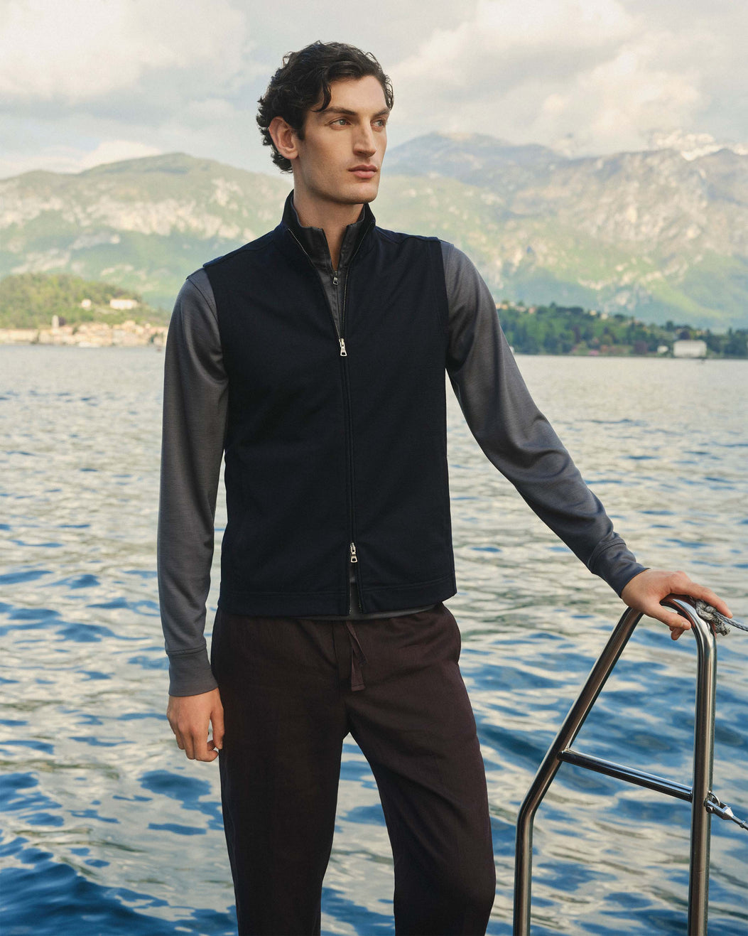 Man standing on a boat with a scenic background of water and mountains