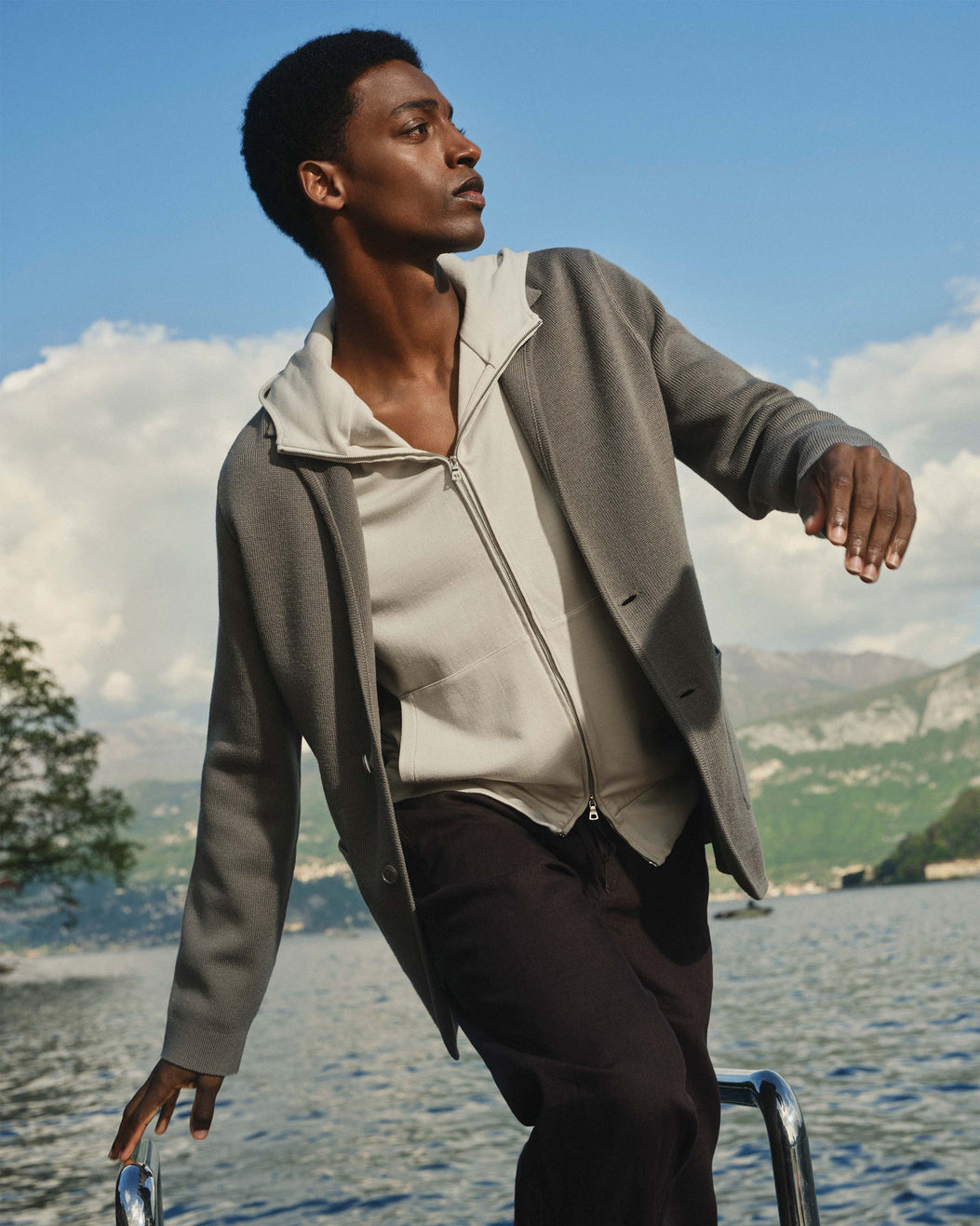 Man in a gray coat standing by a lake with mountains in the background