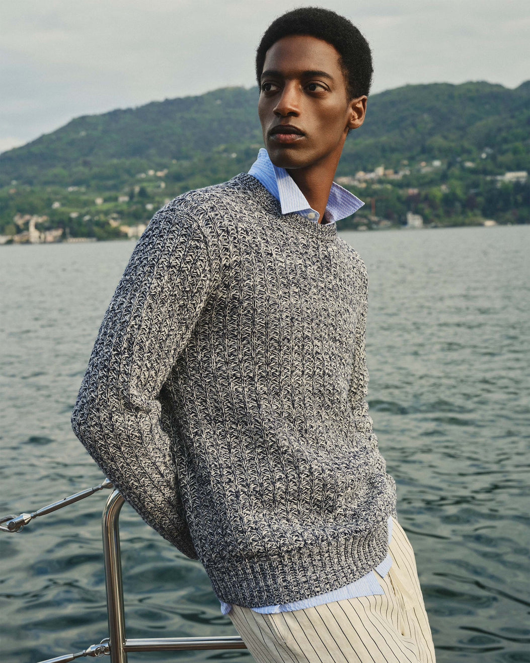 Man wearing a textured sweater by a body of water with mountains in the background