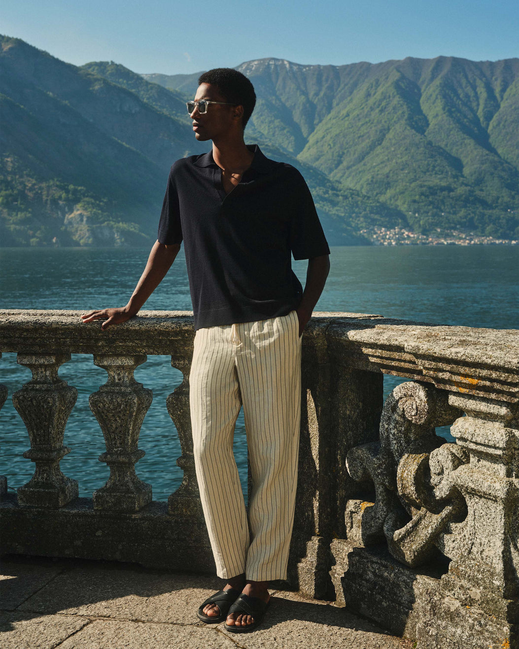 Man standing on a stone balcony overlooking a lake with mountains in the background