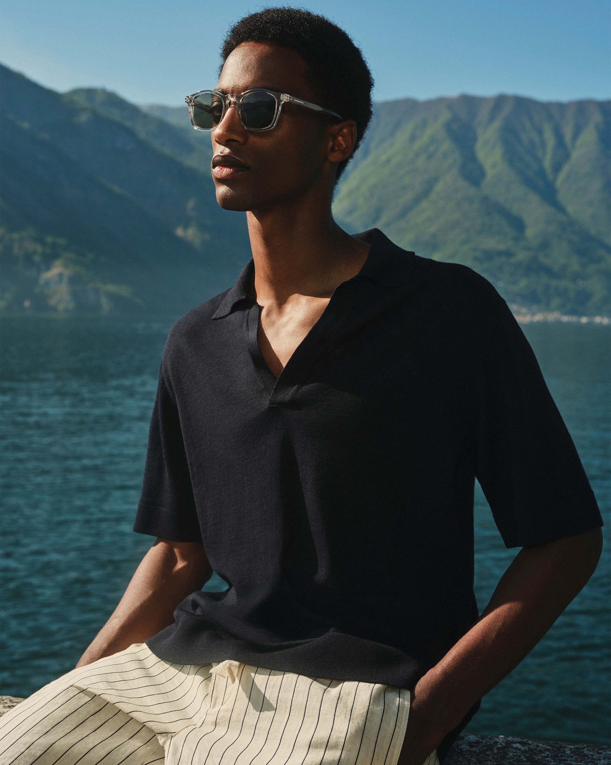 Man wearing sunglasses and a black shirt with mountains and water in the background