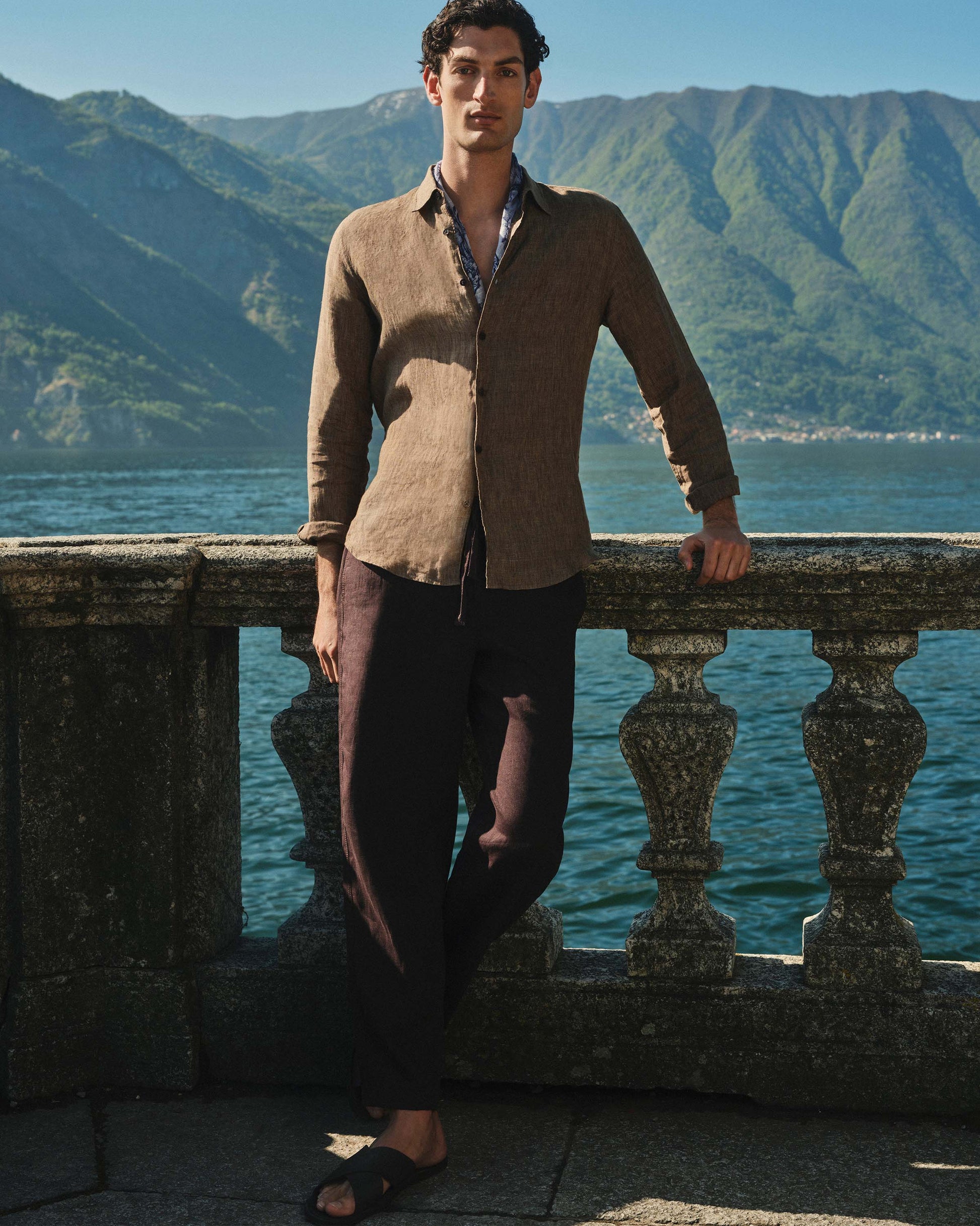 Man standing by a railing with mountains and water in the background