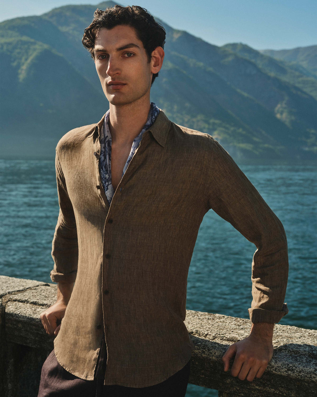 Man standing by a scenic lakeside with mountains in the background