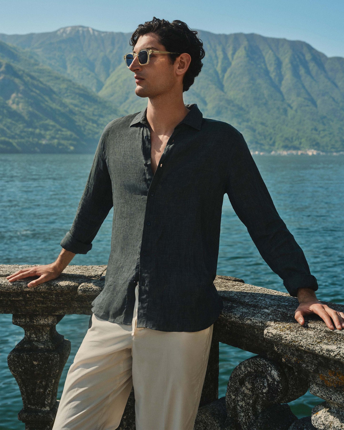 Man standing by a railing with mountains and water in the background
