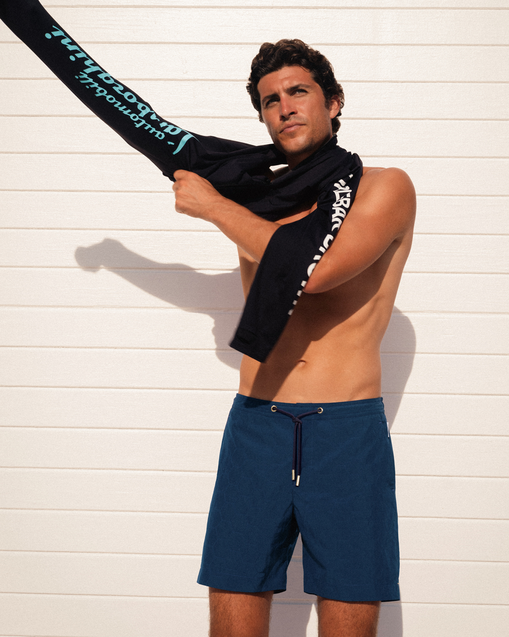 Man putting on a black rashguard with branding against a white wall