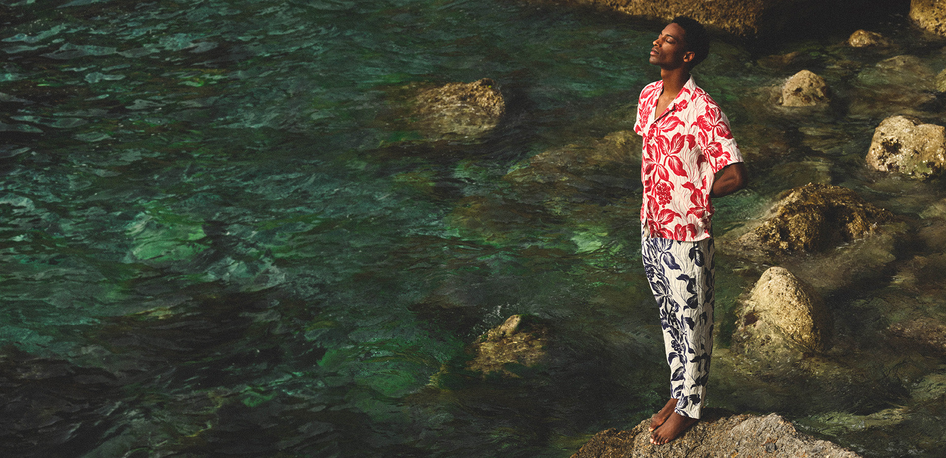 Man wearing floral shirt and trousers on a rock looking out to sea