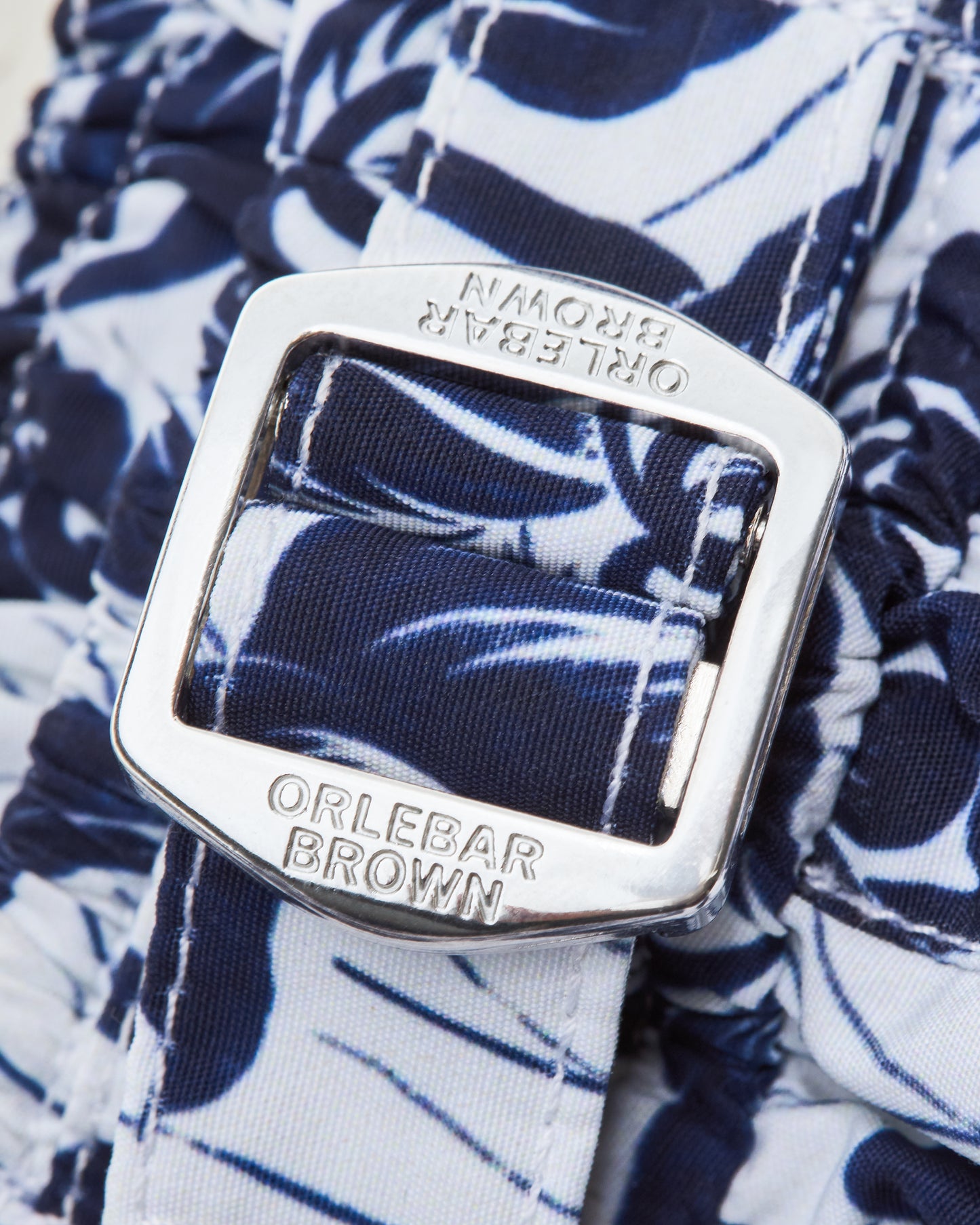 Close-up of an Orlebar Brown belt buckle on a floral-patterned short