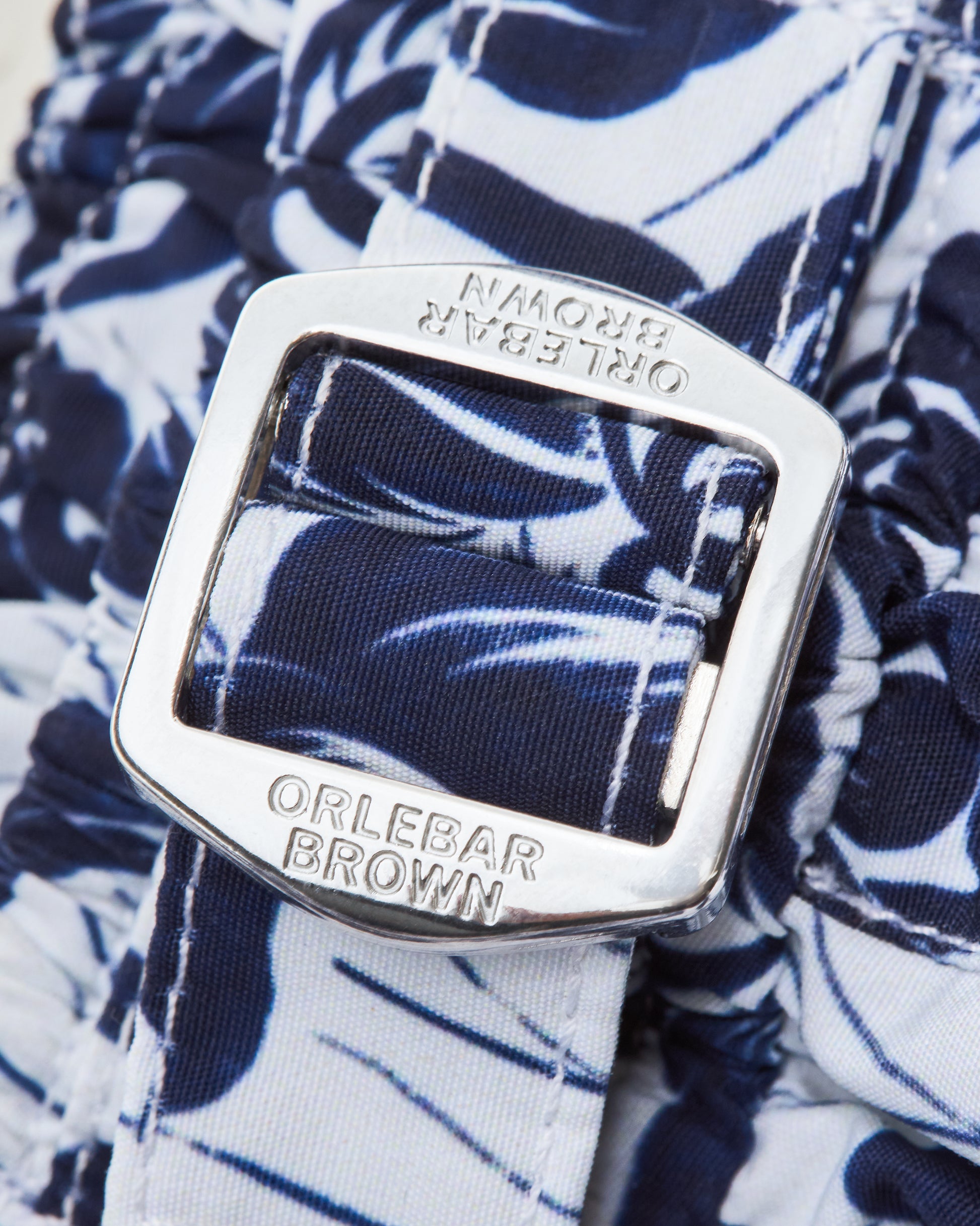 Close-up of an Orlebar Brown belt buckle on a floral-patterned short