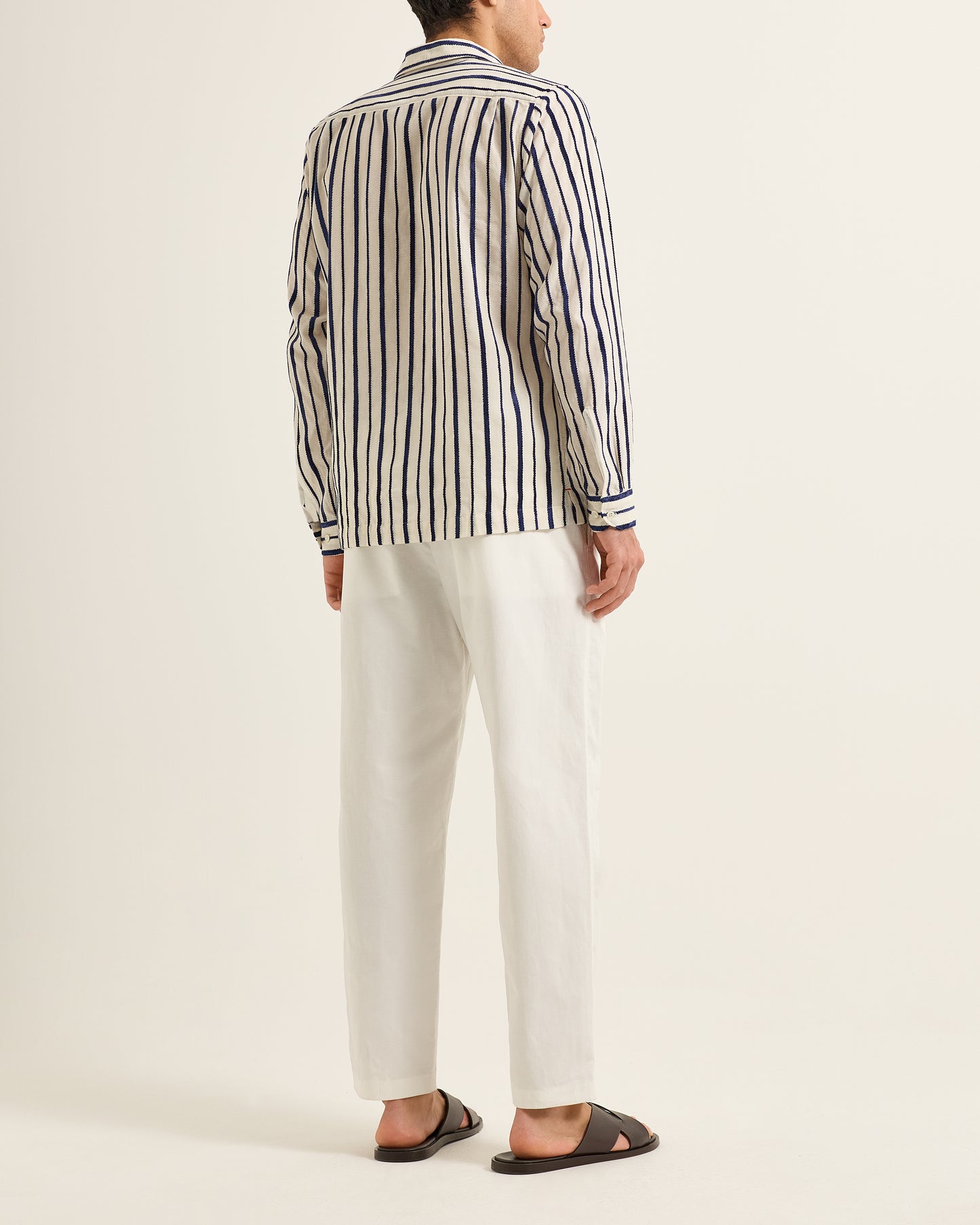 Person wearing a striped shirt and white pants on a plain background