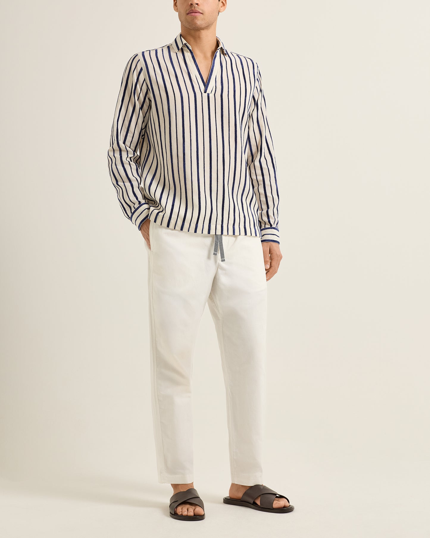 Person wearing a striped shirt and white pants on a plain background