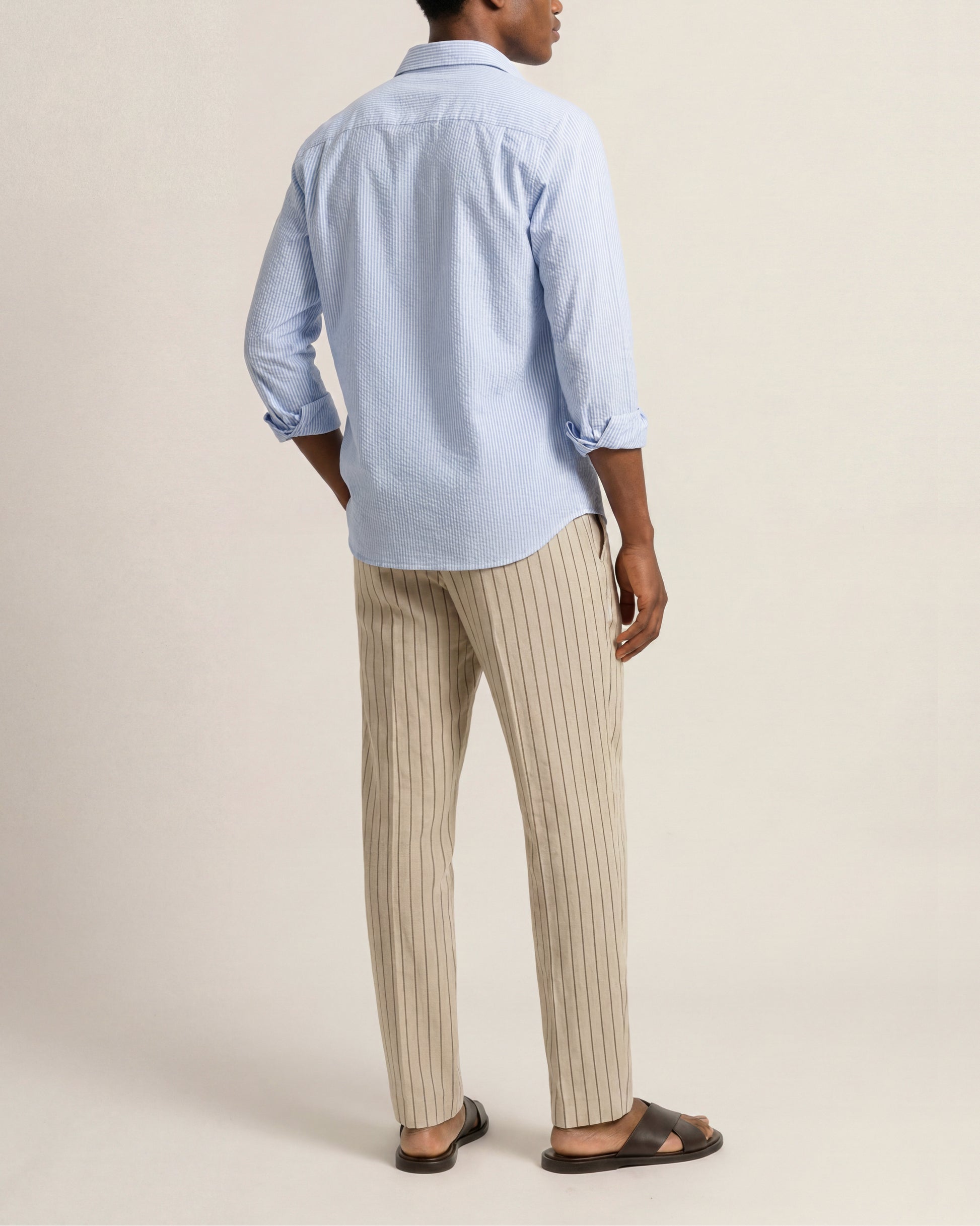 Person wearing a light blue shirt and beige striped pants on a plain background