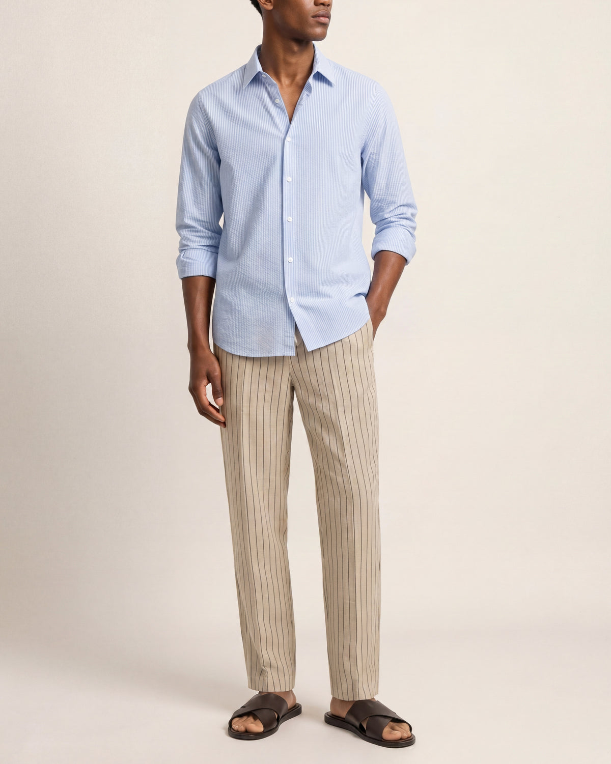 Man wearing a light blue shirt and beige striped pants on a plain background