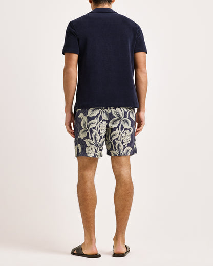 Person wearing a navy polo shirt and floral shorts on a white background