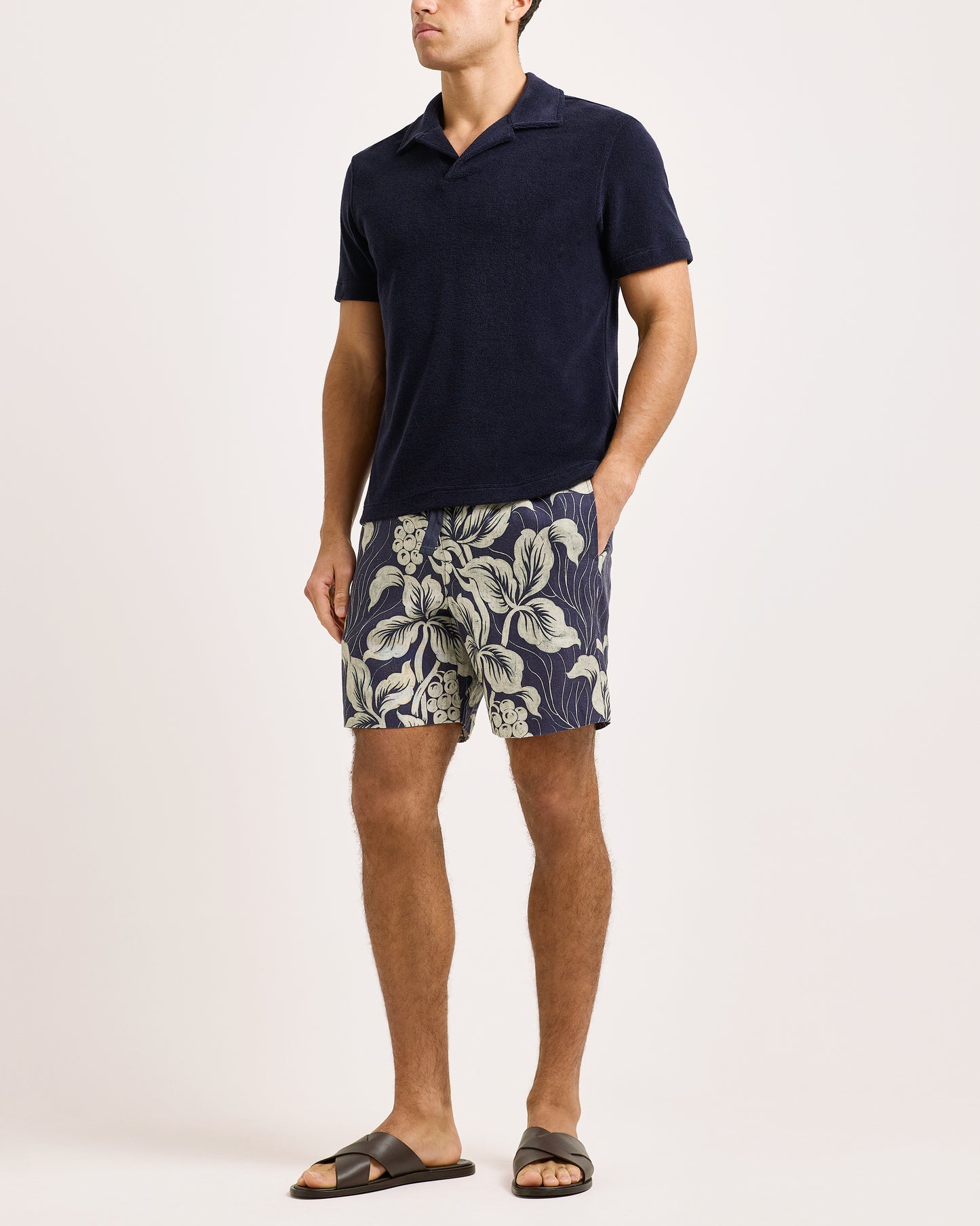 Man wearing navy polo shirt and leaf-patterned shorts on a white background