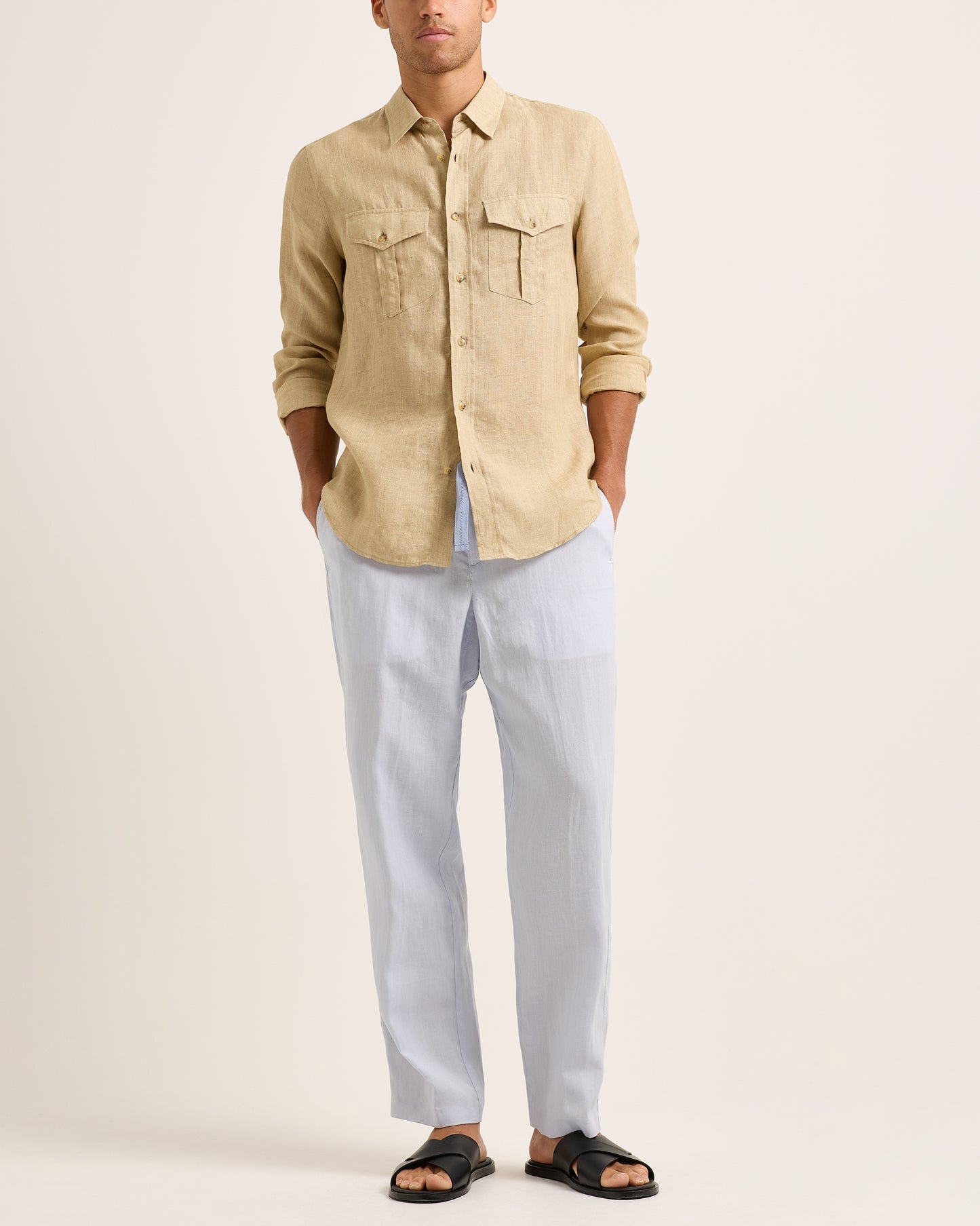 Person wearing a beige shirt and light blue trousers with a blue drawstring on a white background